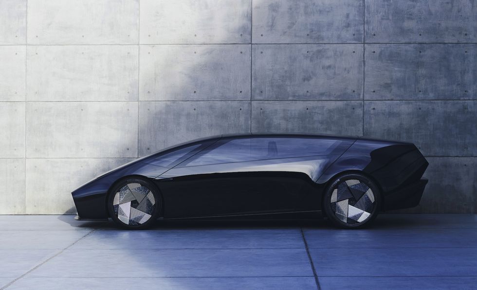 Low, sleek black futuristic car parked beside a concrete wall.