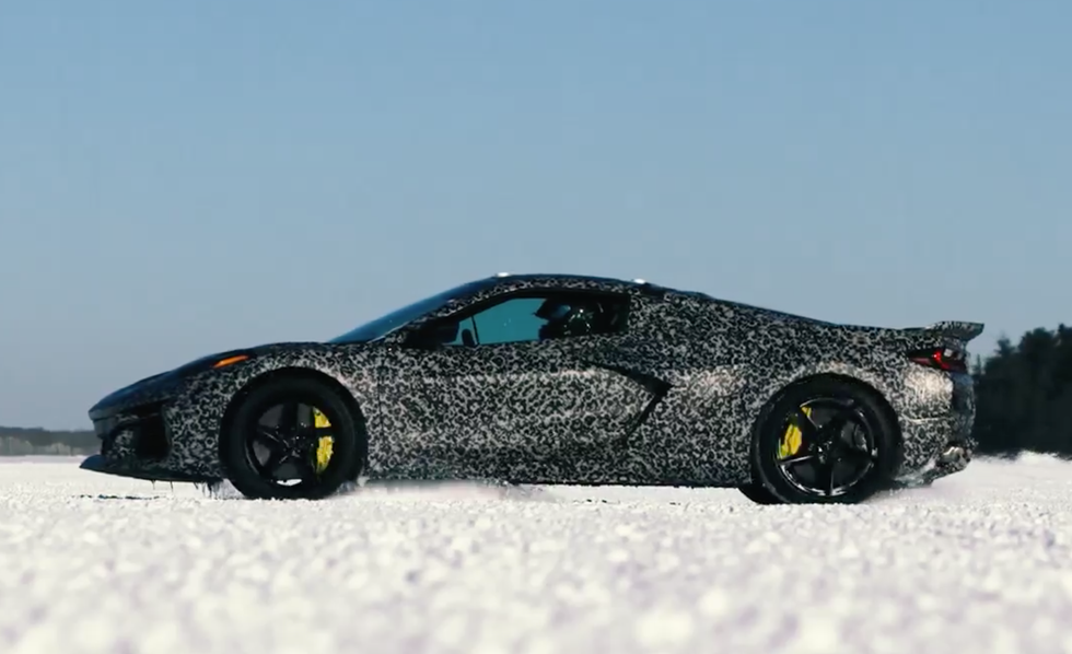 Camouflaged sports car driving on snow under a clear blue sky