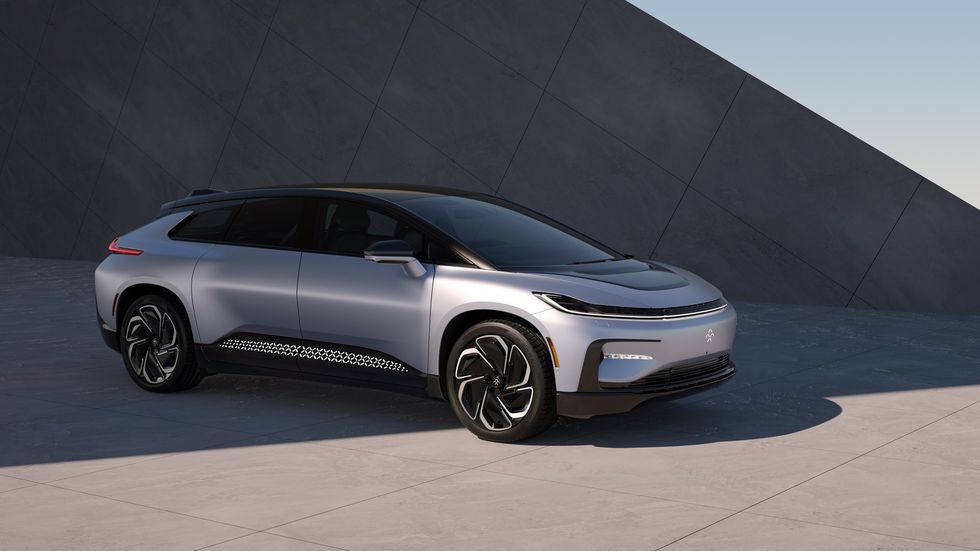 Silver futuristic SUV concept car parked on pavement beside a dark geometric wall.