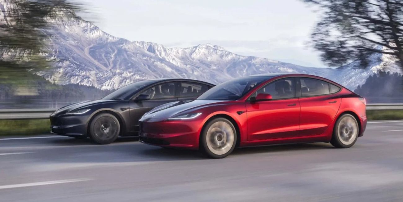 Two Tesla sedans, black and red, driving side by side on a scenic snowy road