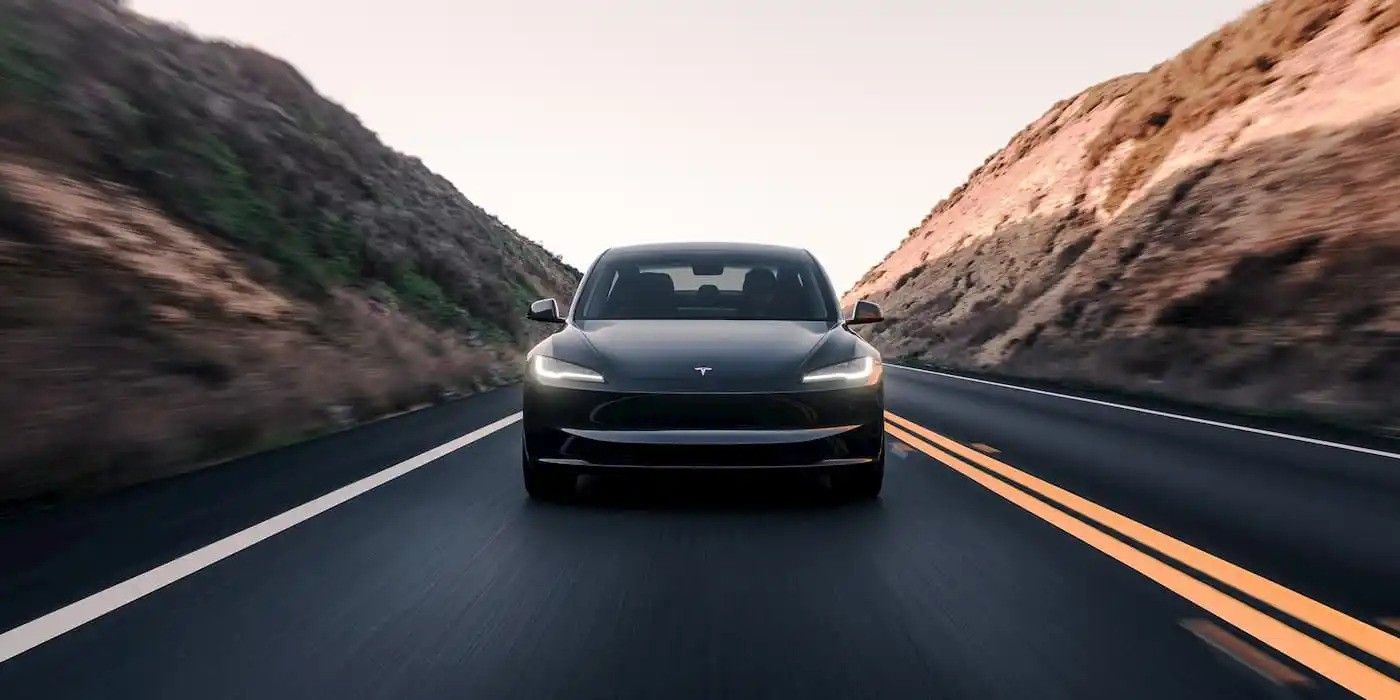 Front view of a black car driving on a winding road between rocky hills at sunset