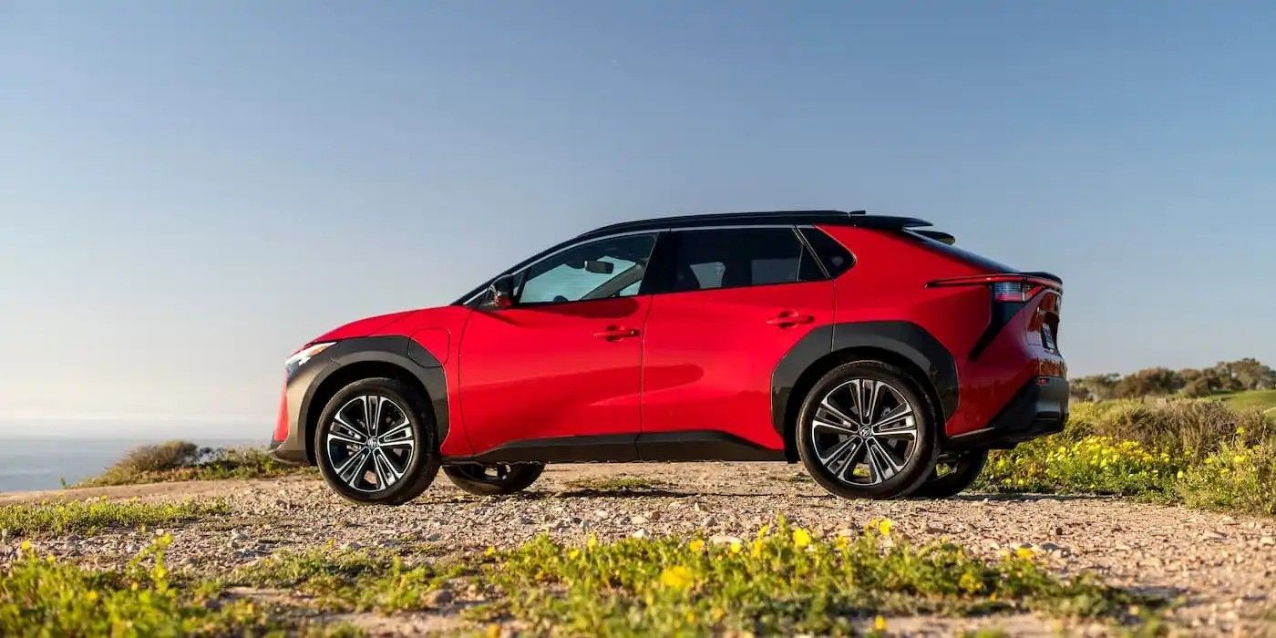 Red SUV parked on a rocky hilltop with ocean and sky in the background.