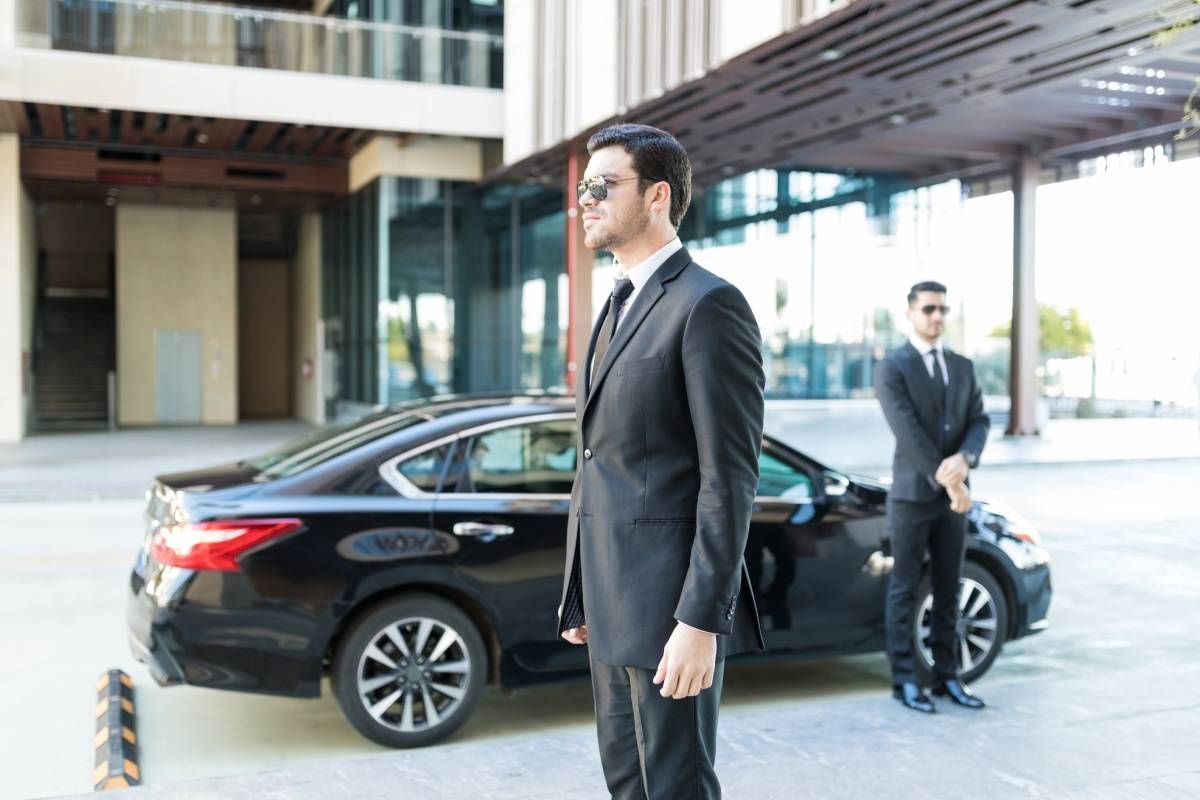 Two agents providing private security services for a client outside of a car.