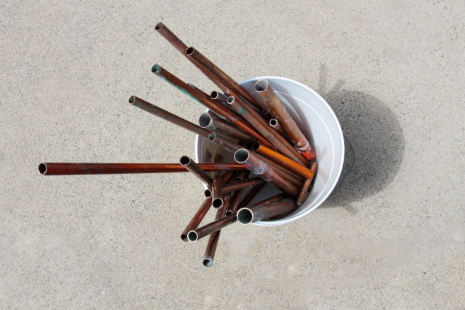 Tubes in a white bucket on concrete, many rusty brown, some with silver ends, top view.