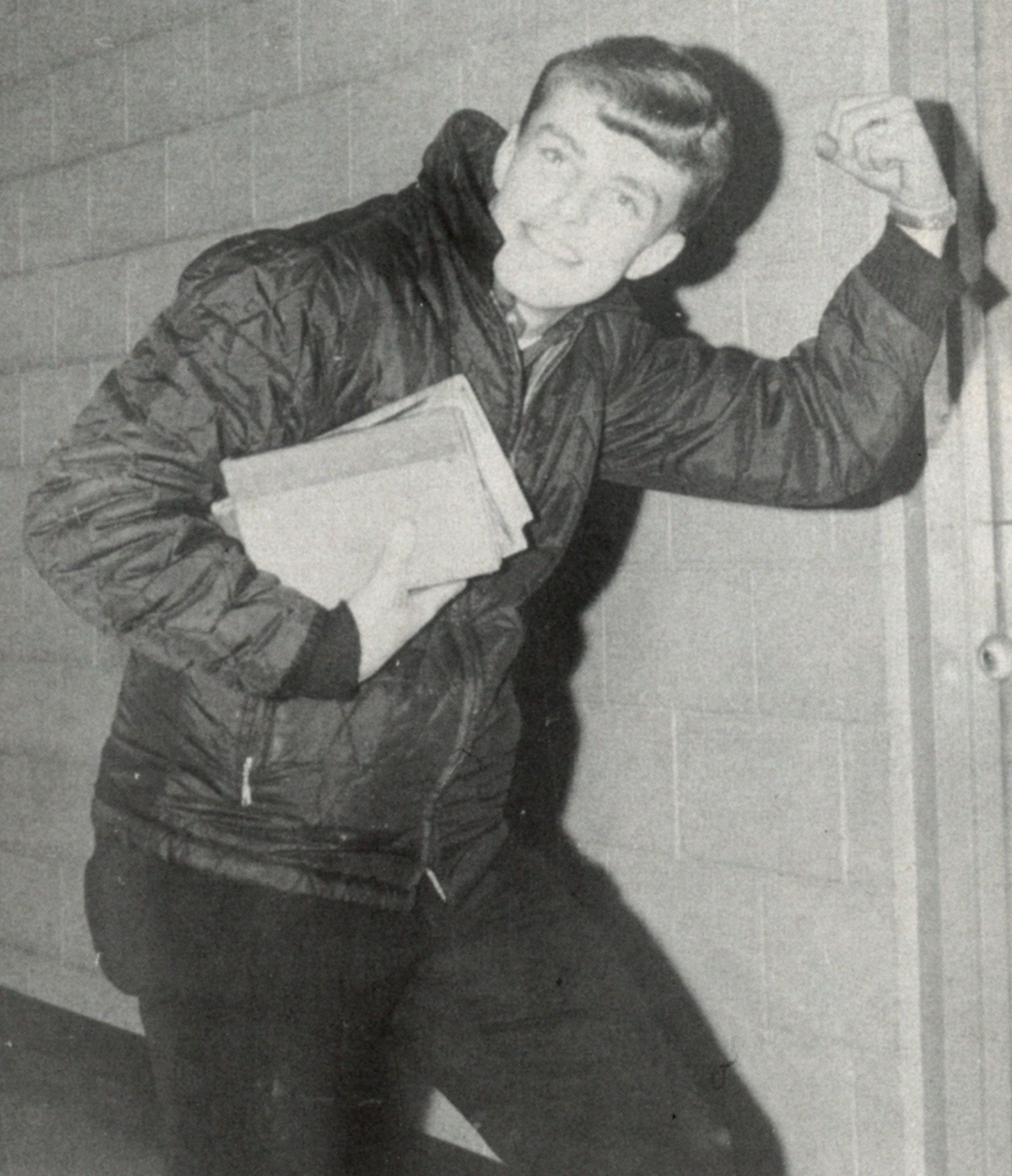 Smiling guy wearing a jacket, posing with one arm flexed and the other arm holding small notebooks.