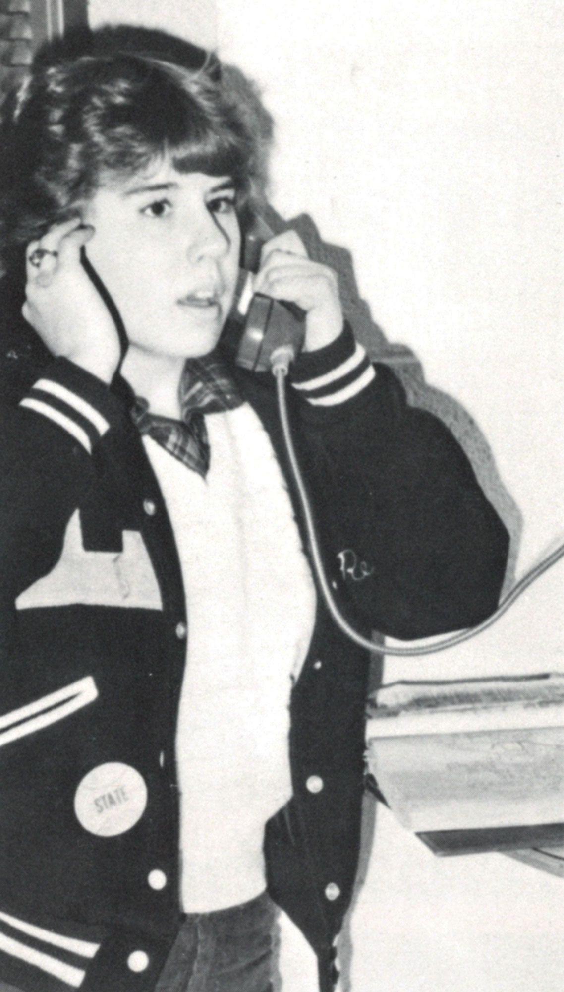 Female student in a letter jacket, on a pay phone