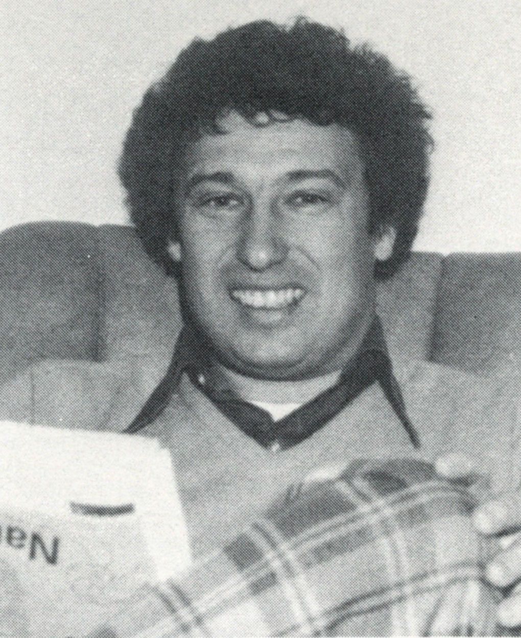 Mr. Gauger, sitting on sofa or chair, holding a newspaper, and smiling at the camera
