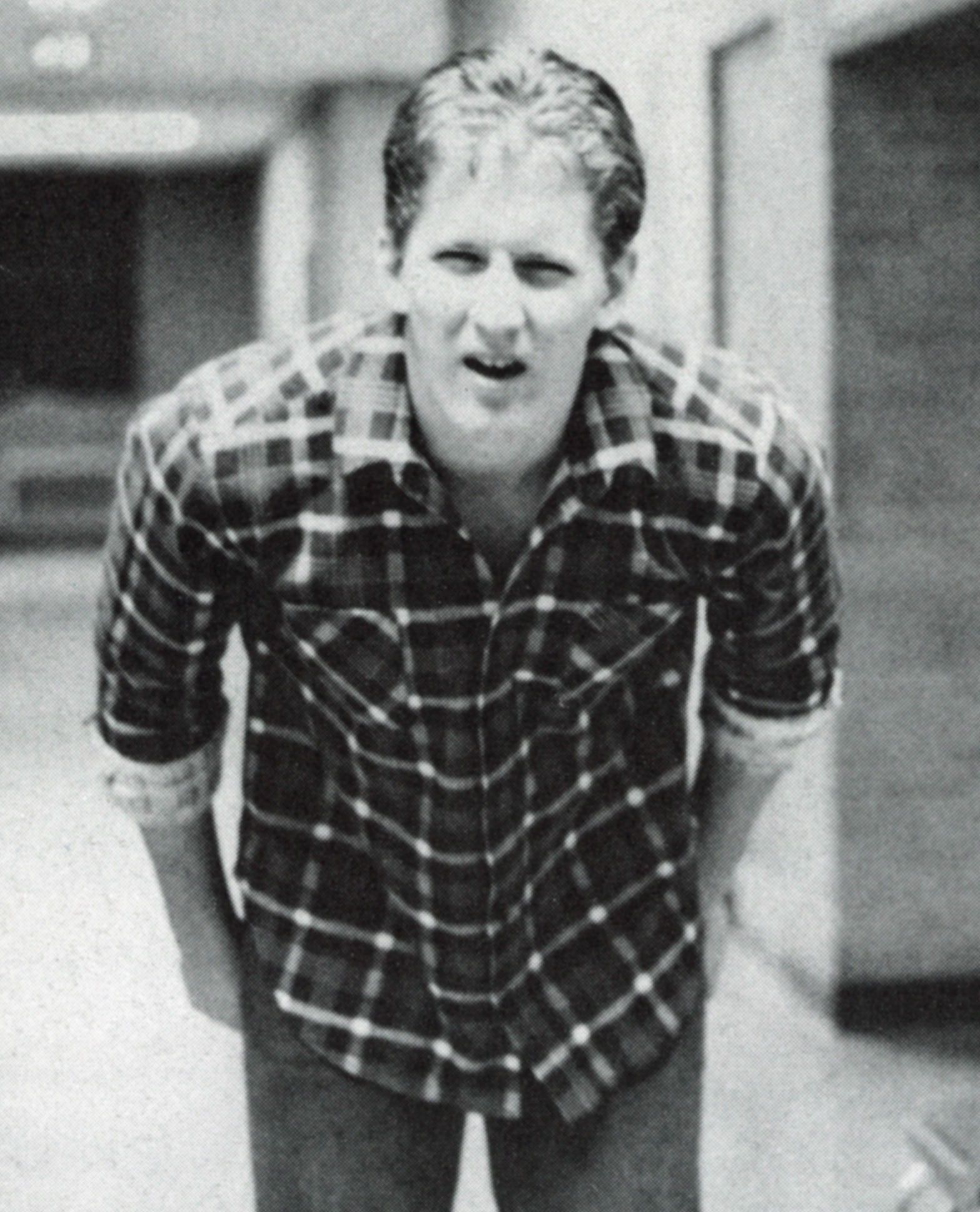 Male student in the hallway, with his hands behind him, and leaning toward the photographer