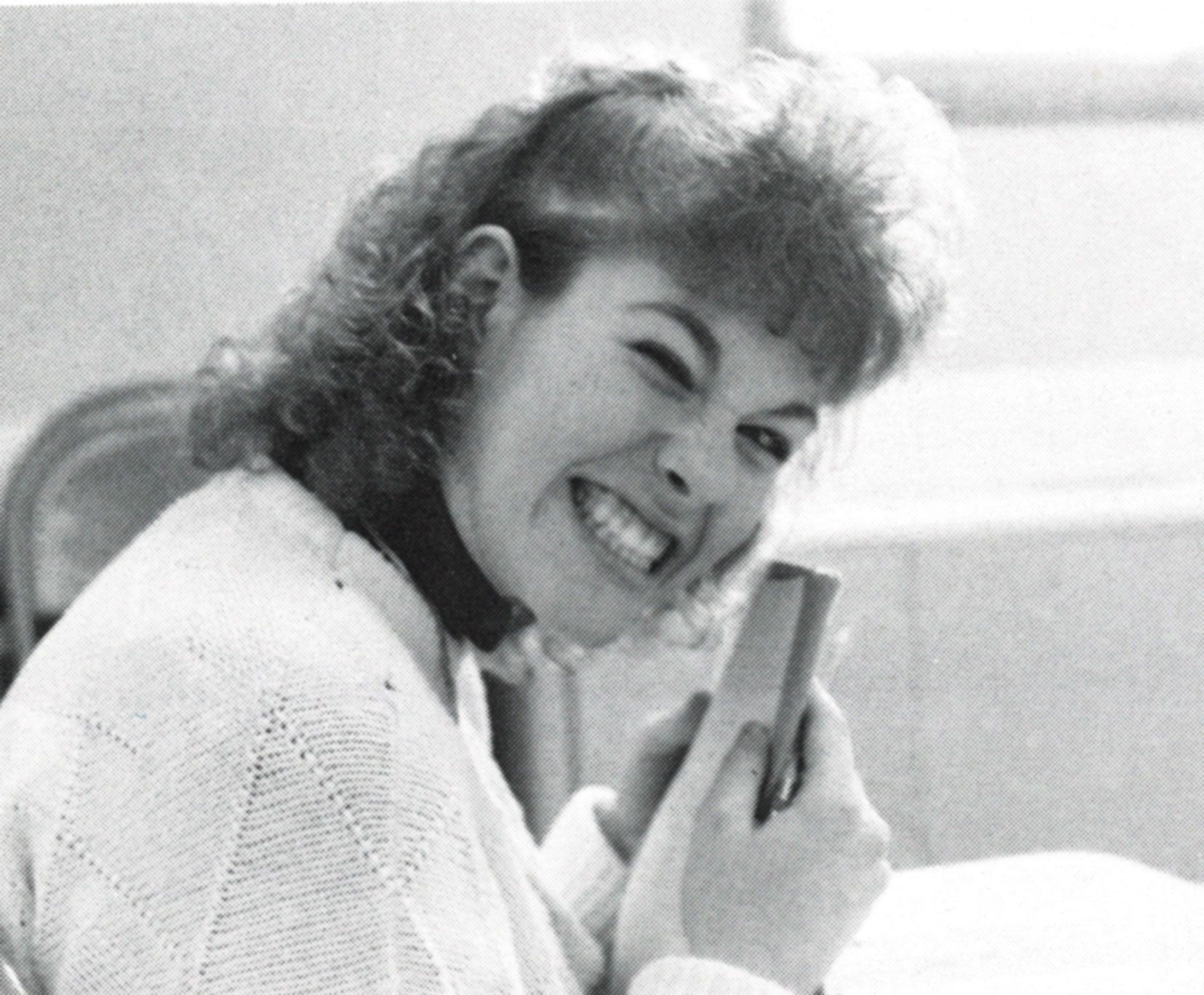 Female student smiling, sitting at a desk, and holding a small book