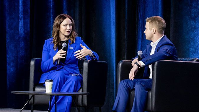 Erin sitting in a chair on stage, talking in a microphone - male interviewer is in chair next to her