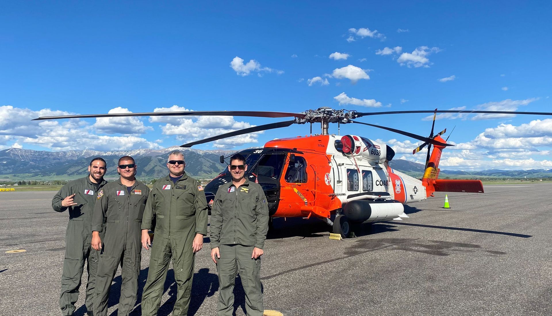 Jon with three other crew members in front of a Coast Guard helicopter with the Bozeman, Montana mountains in the background
