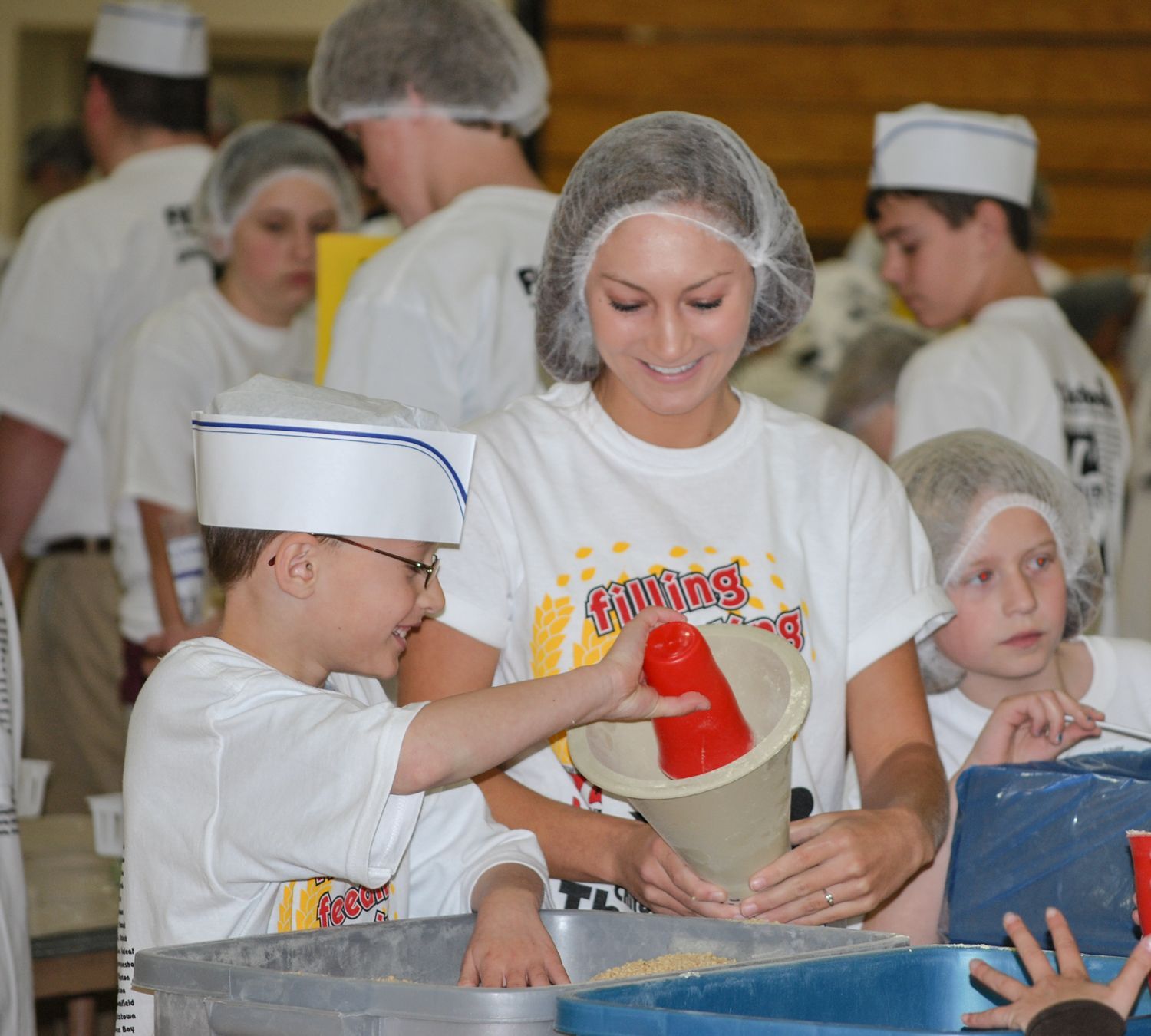 High school student helping two grade school students during the Children Feeding Thousands event