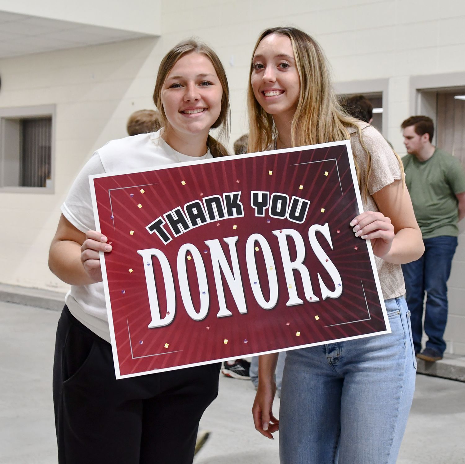 Two smiling girls in the FVL hallway, holding a sign that says 