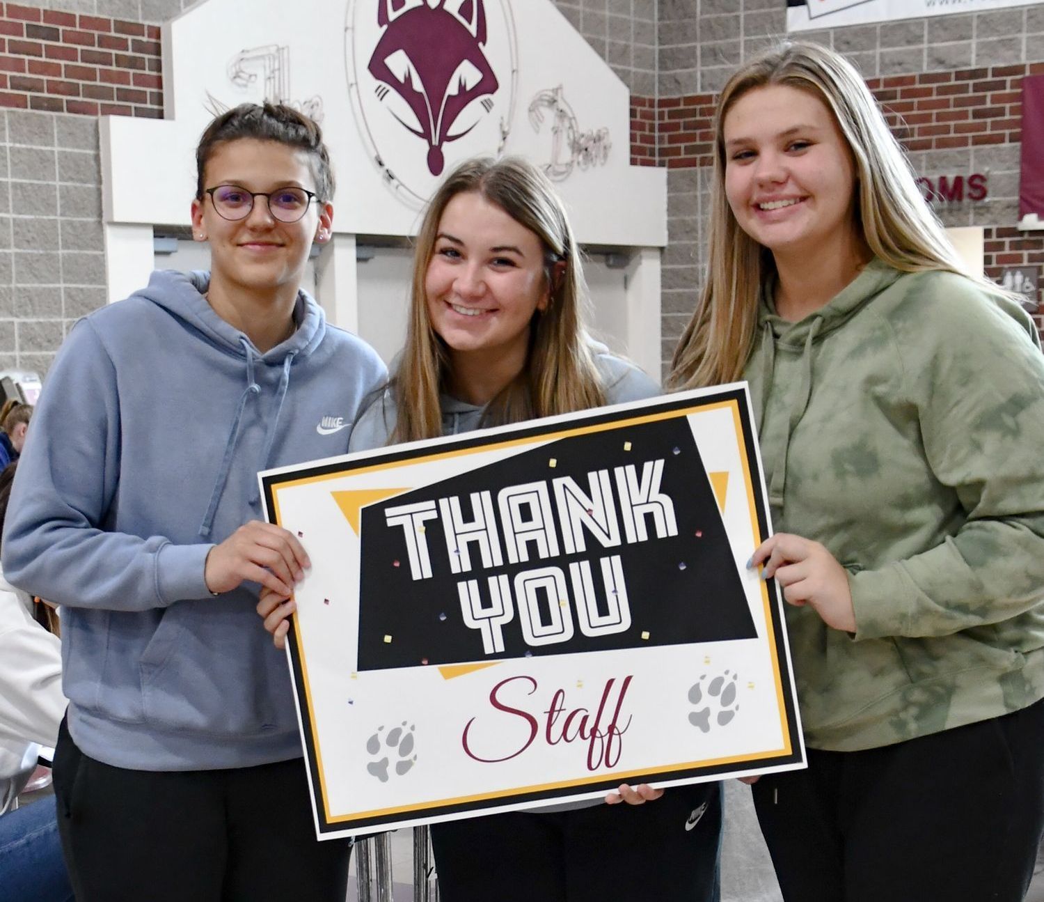 Three smiling students in Commons holding a sign that says