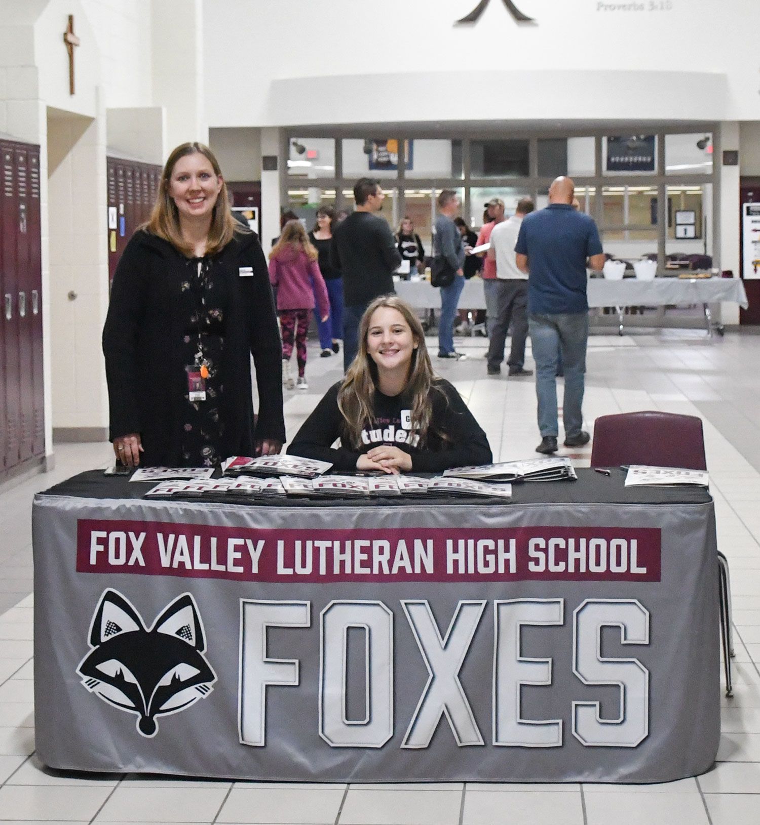 Staff member and student at an FVL Foxes table, greeting visitors