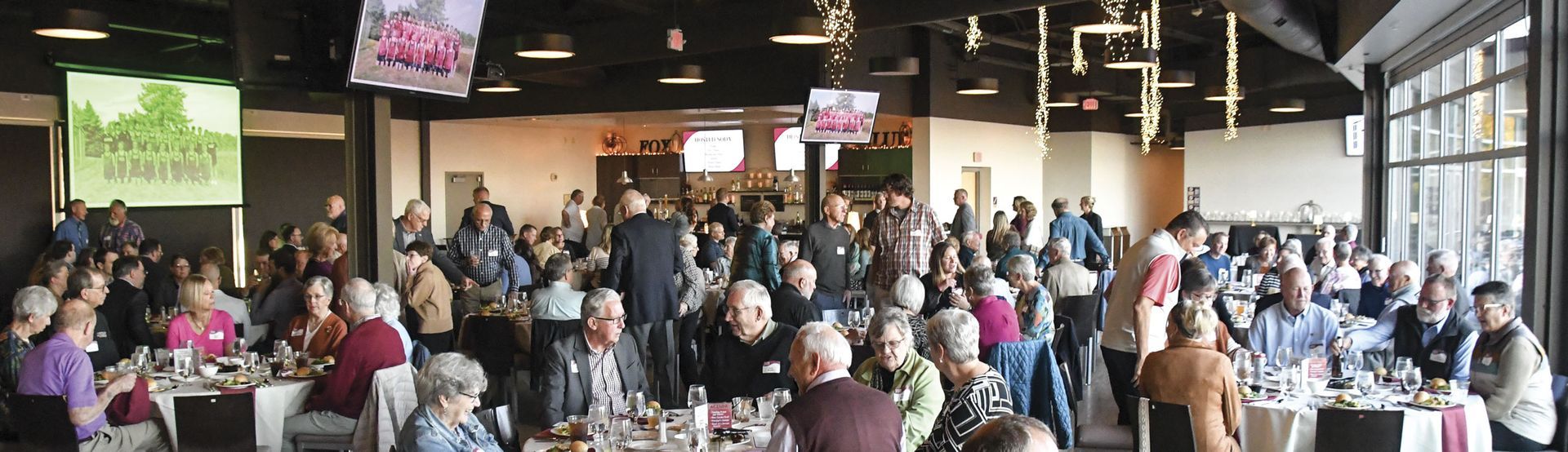 Broad view of windowed room with many tables filled with guests, ready to eat