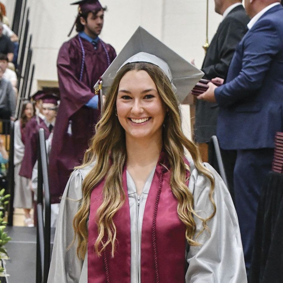 Smiling female graduate in cap and gown, after walking off the stage with her diploma