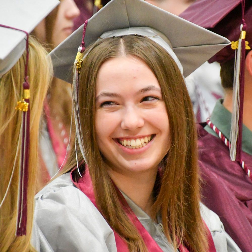 Female graduate, sitting in her chair, smiling at the person next to her