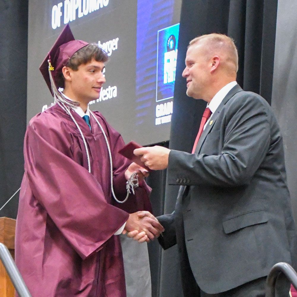 Smiling student, pointing at diploma, as she walks back to her chair