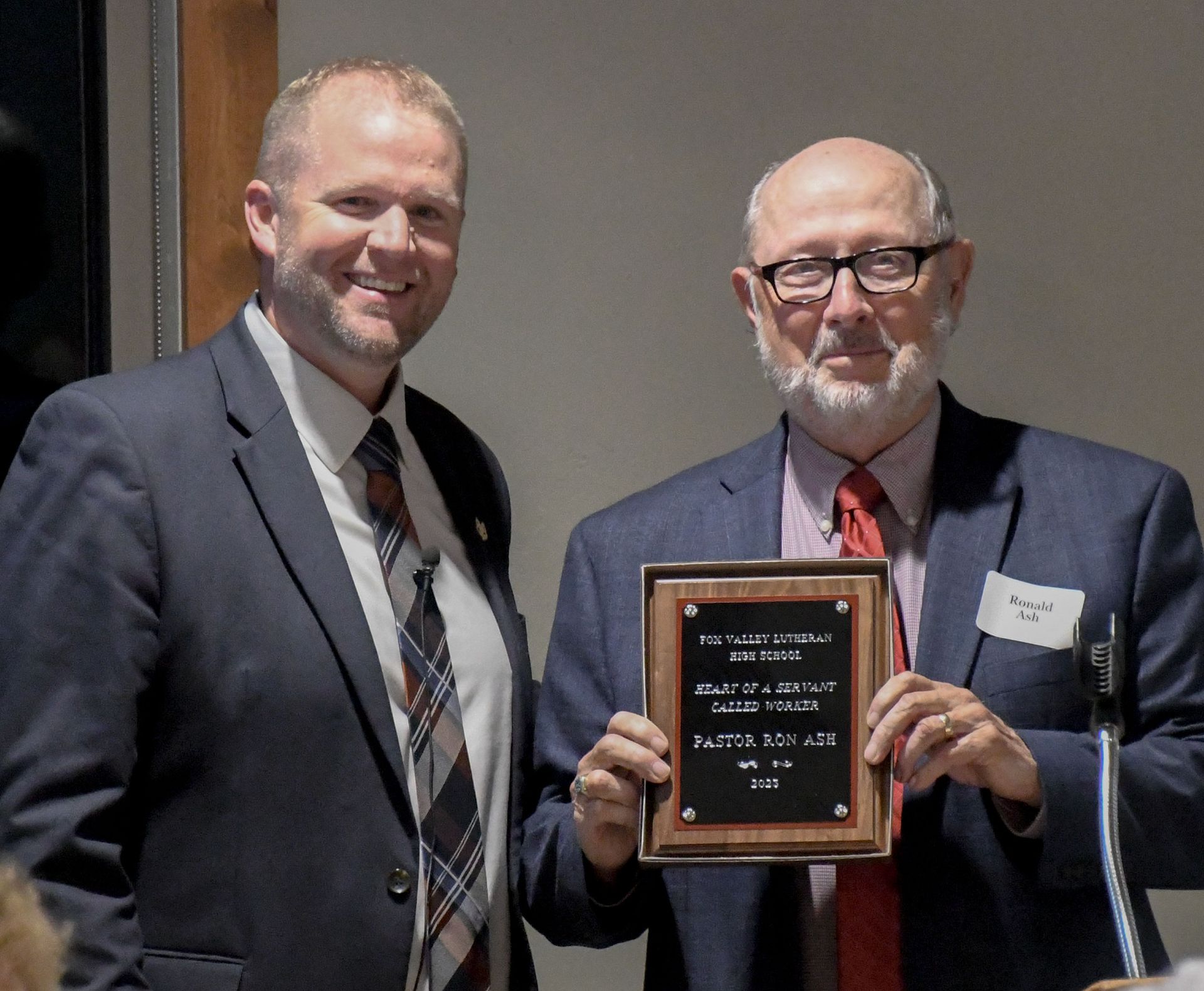 President Loberger smiling and standing by a happy Rev. Ron Ash who is holding up his Heart of a Servant plaque