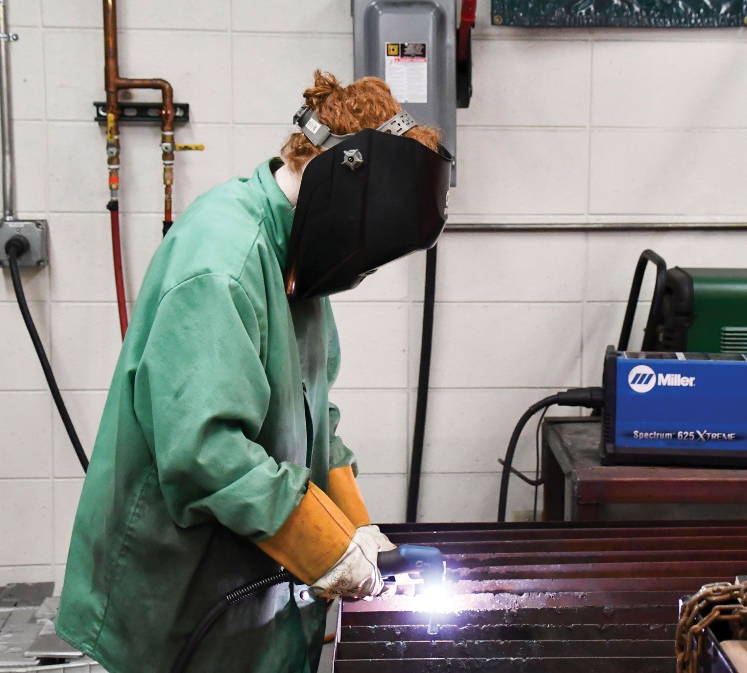 Side view of a student in the metals lab, working. Hood is covering the face.