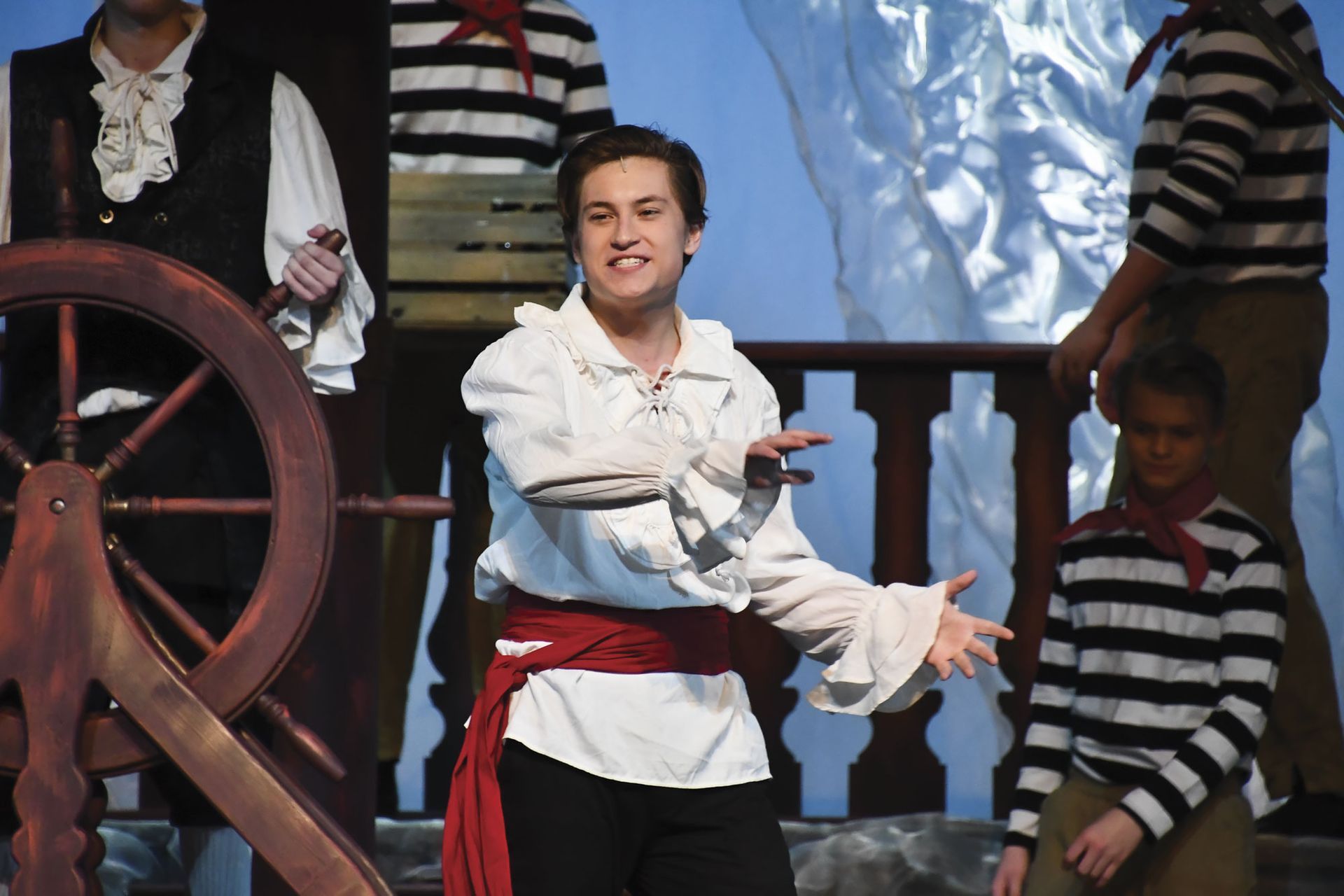 Male on a ship, in a white shirt with a red sash, and singing