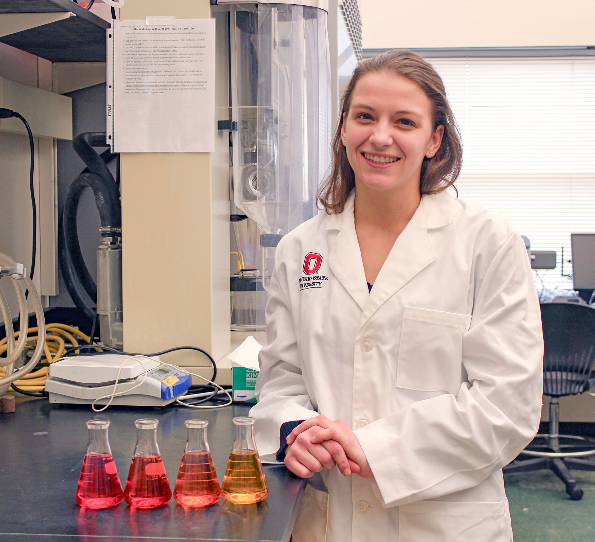 Danielle Voss in lab coat, in science lab with beakers on table in front of her
