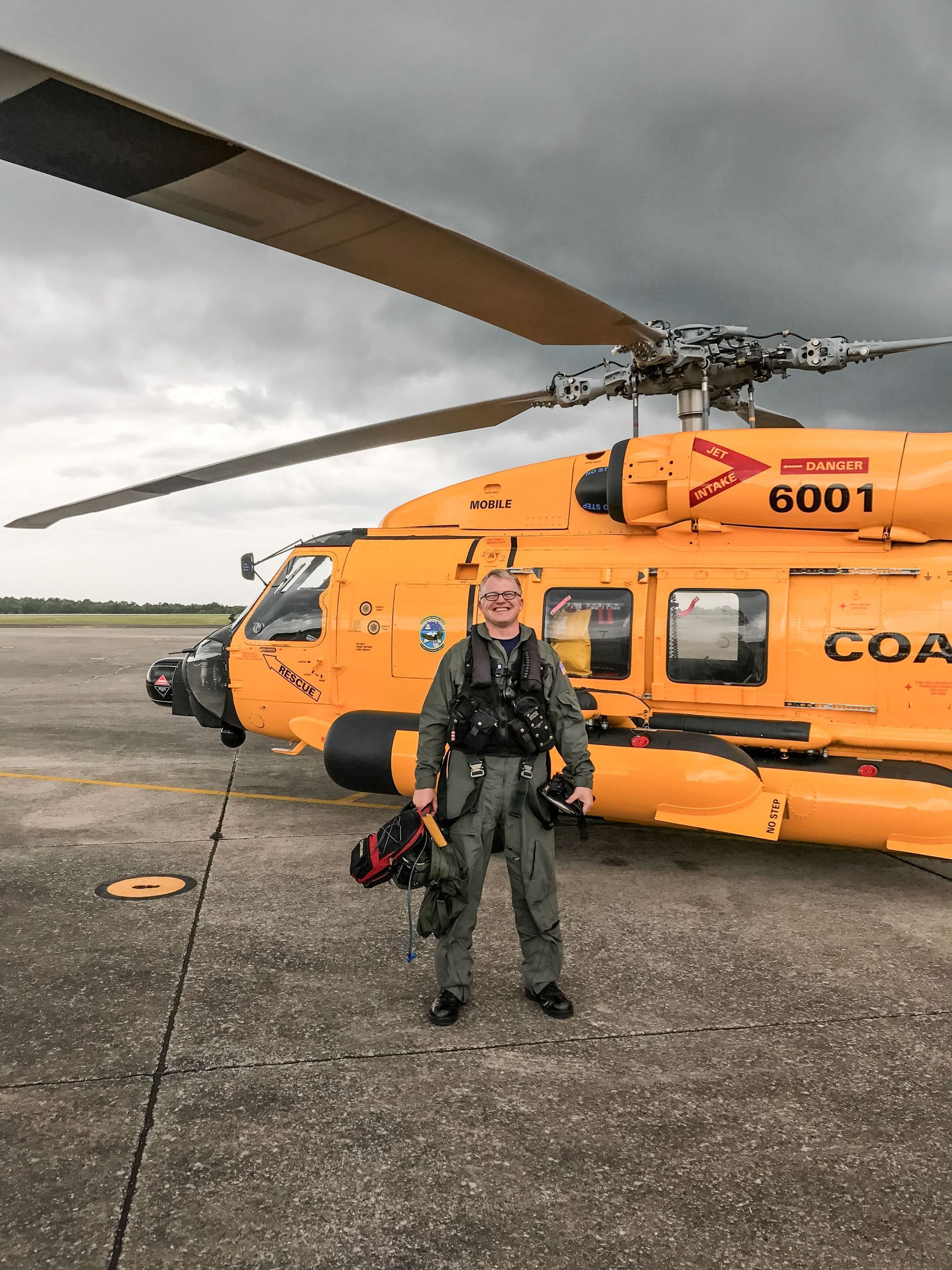 Jon Bartel standing in front of a Coast Guard helicopter with cloudy skies overhead.