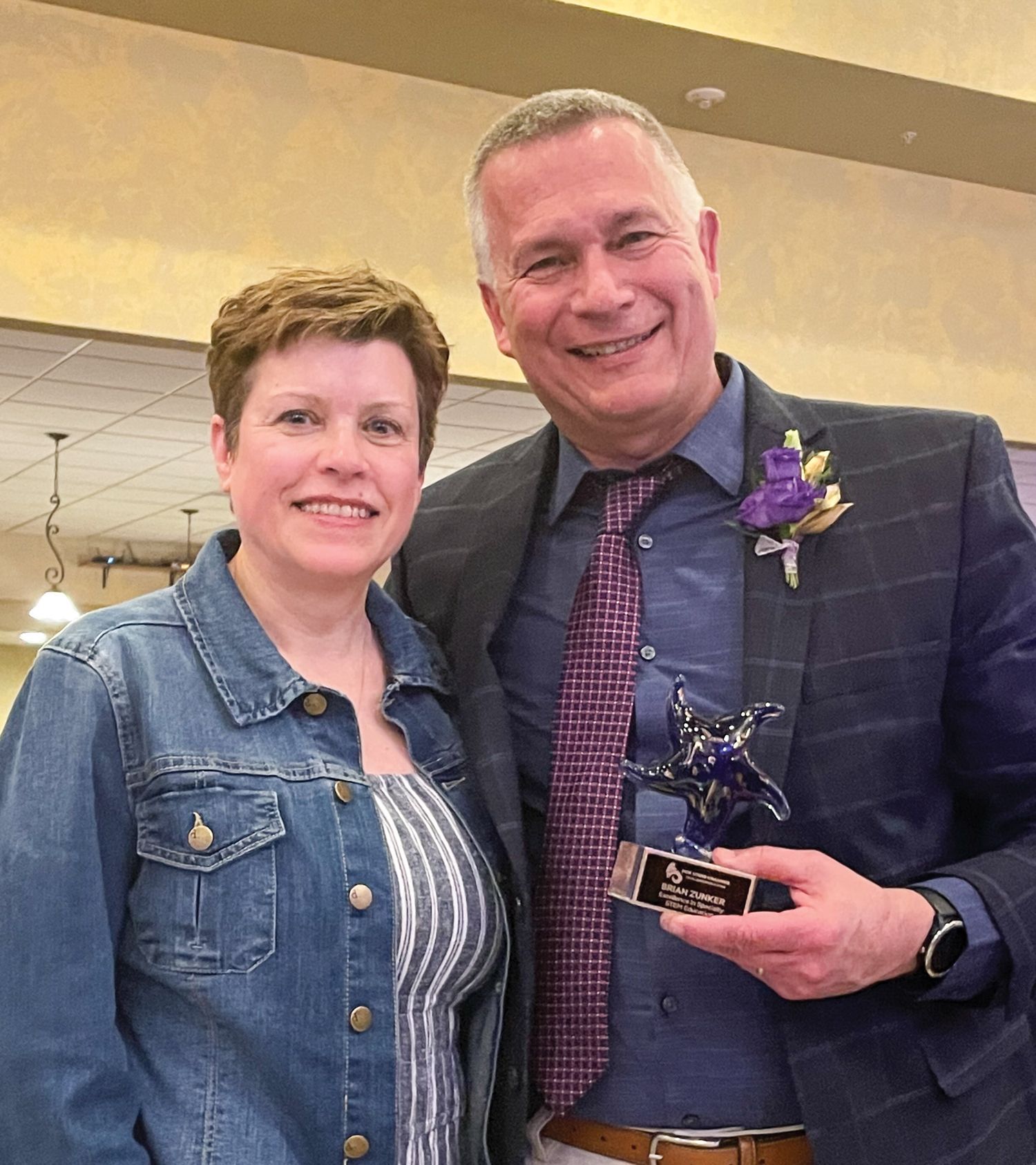 Brian Zunker, holding his Shining Star Award, and wearing a purple flower on his lapel. He has his arm around his wife, Deb
