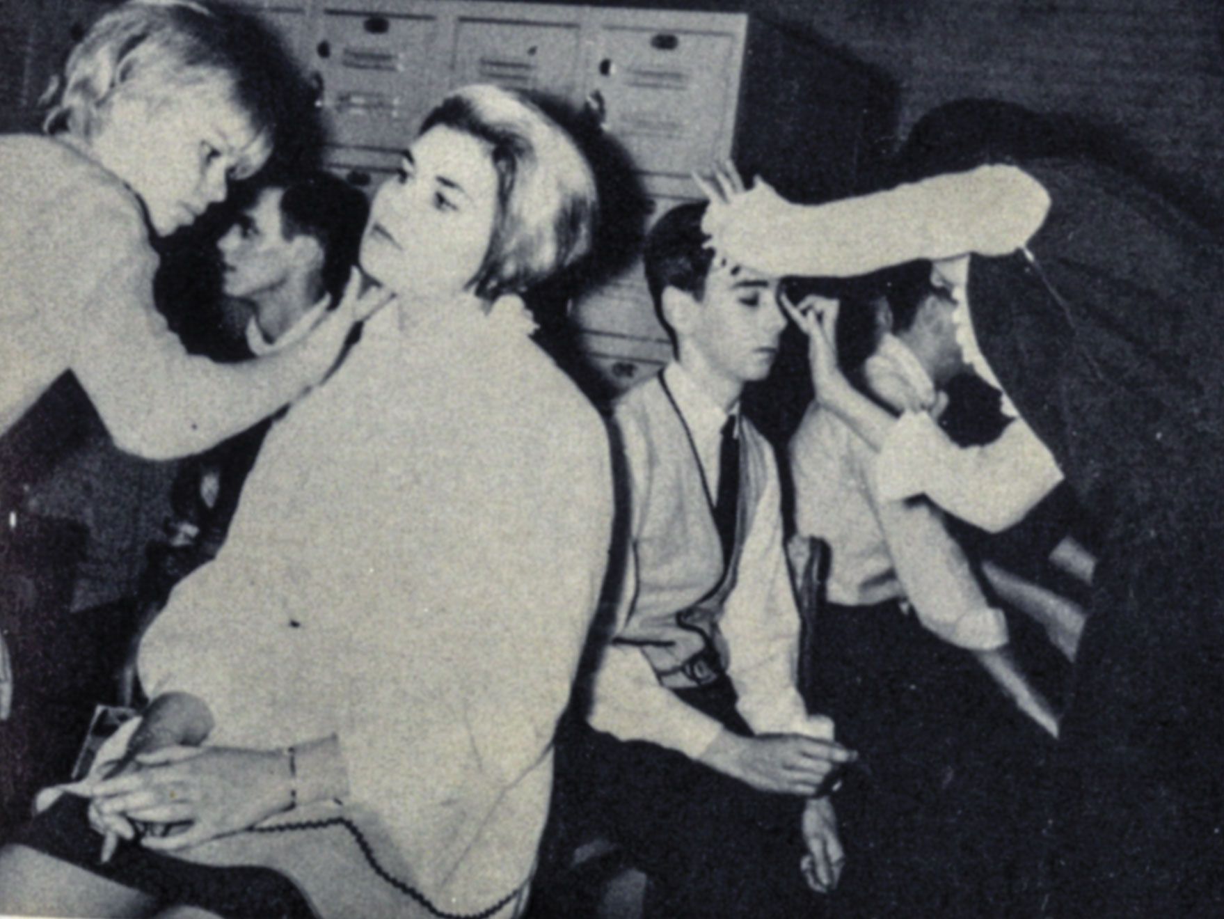 Students sitting in chairs with other students applying make-up