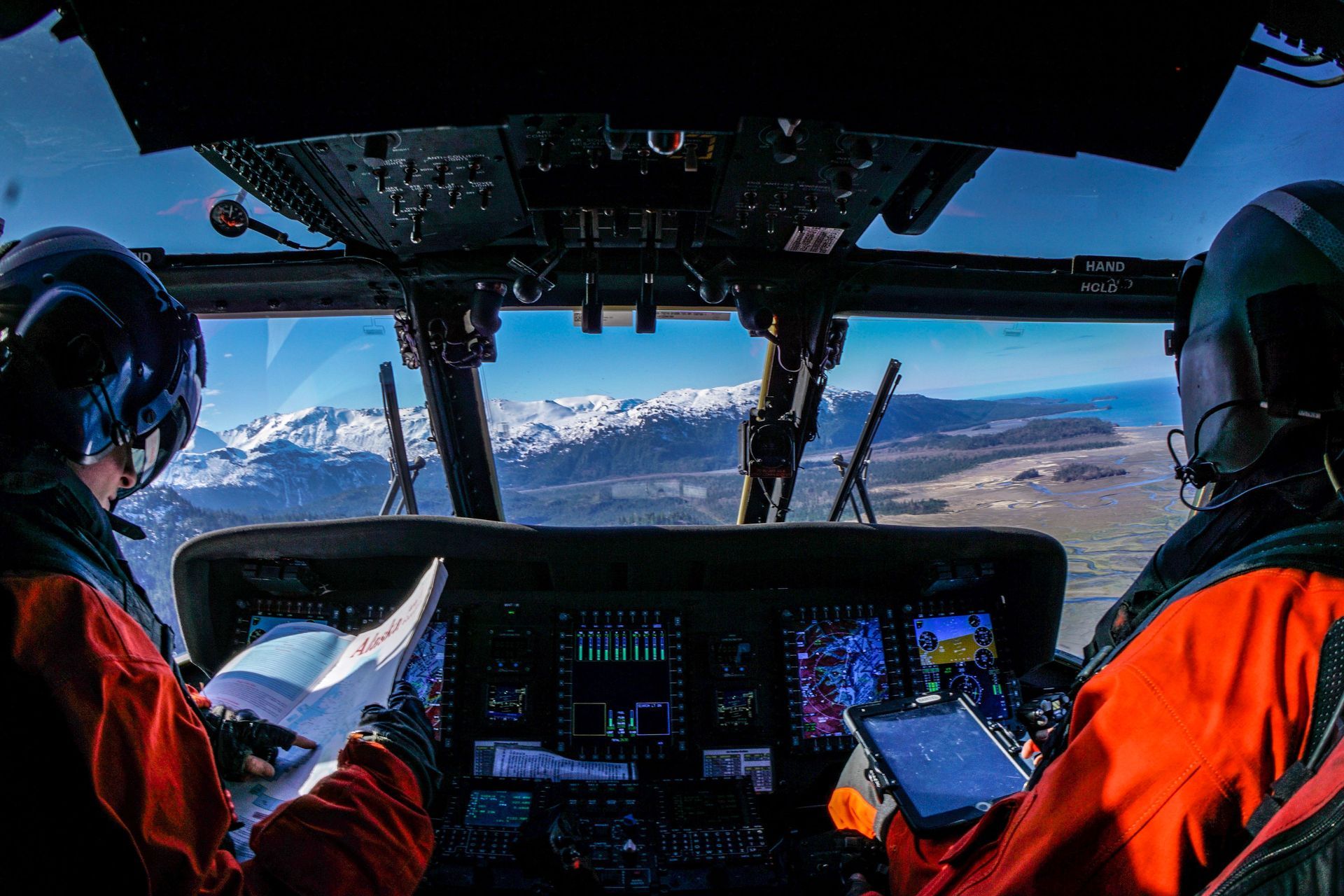 View from inside a Coast Guard helicopter, looking out at the beautiful Alaska mountains over the control panels