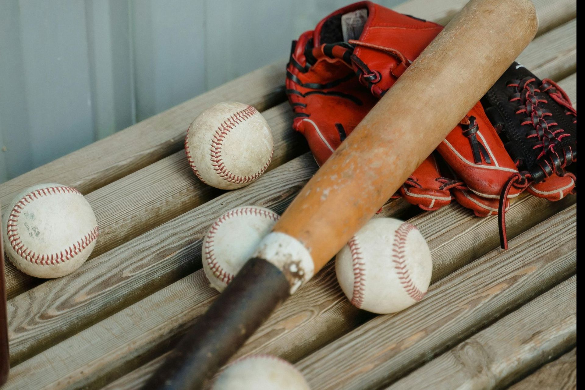Baseball bat, balls, and glove on a wooden bench