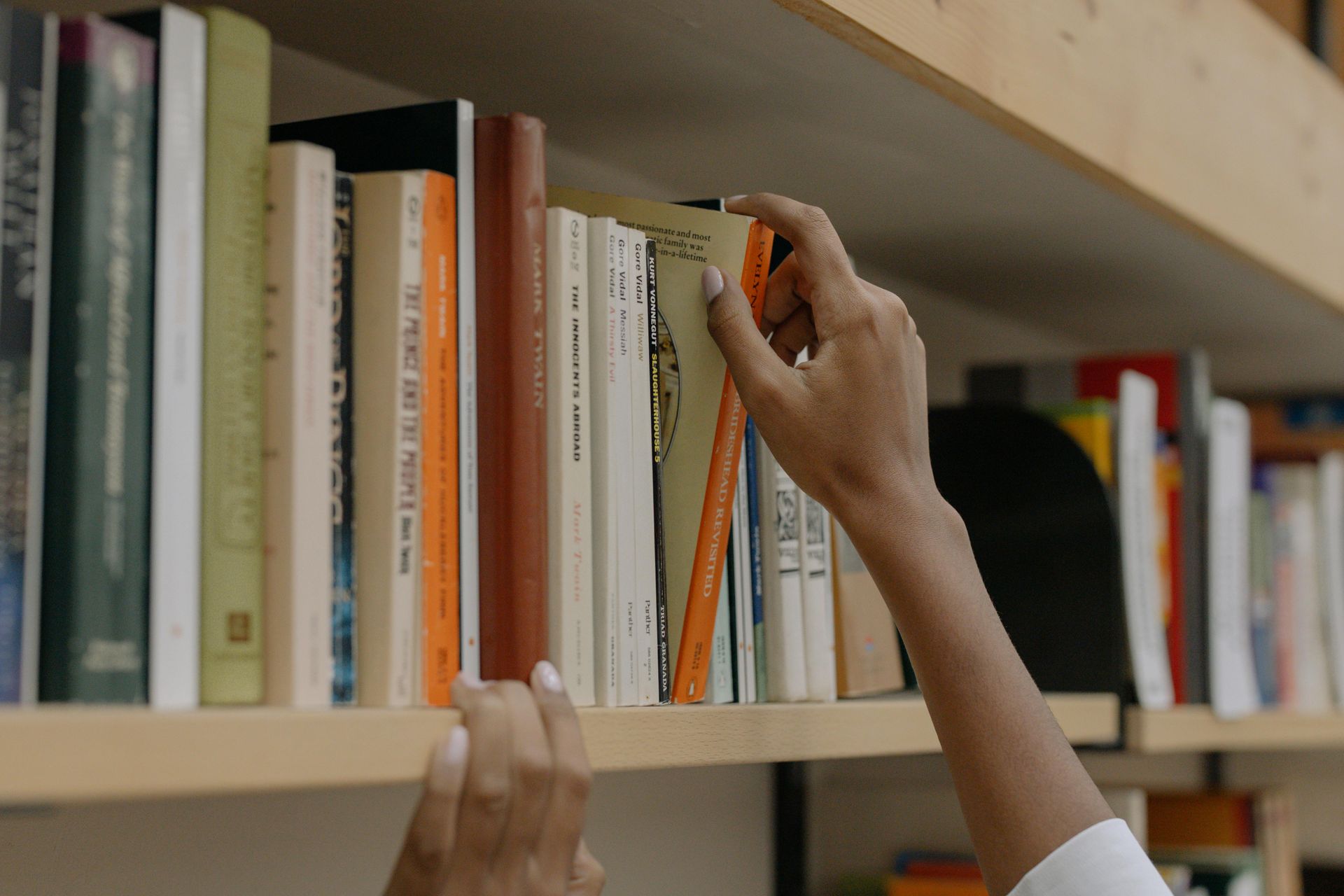 Hand taking book off a well-stocked shelf of books