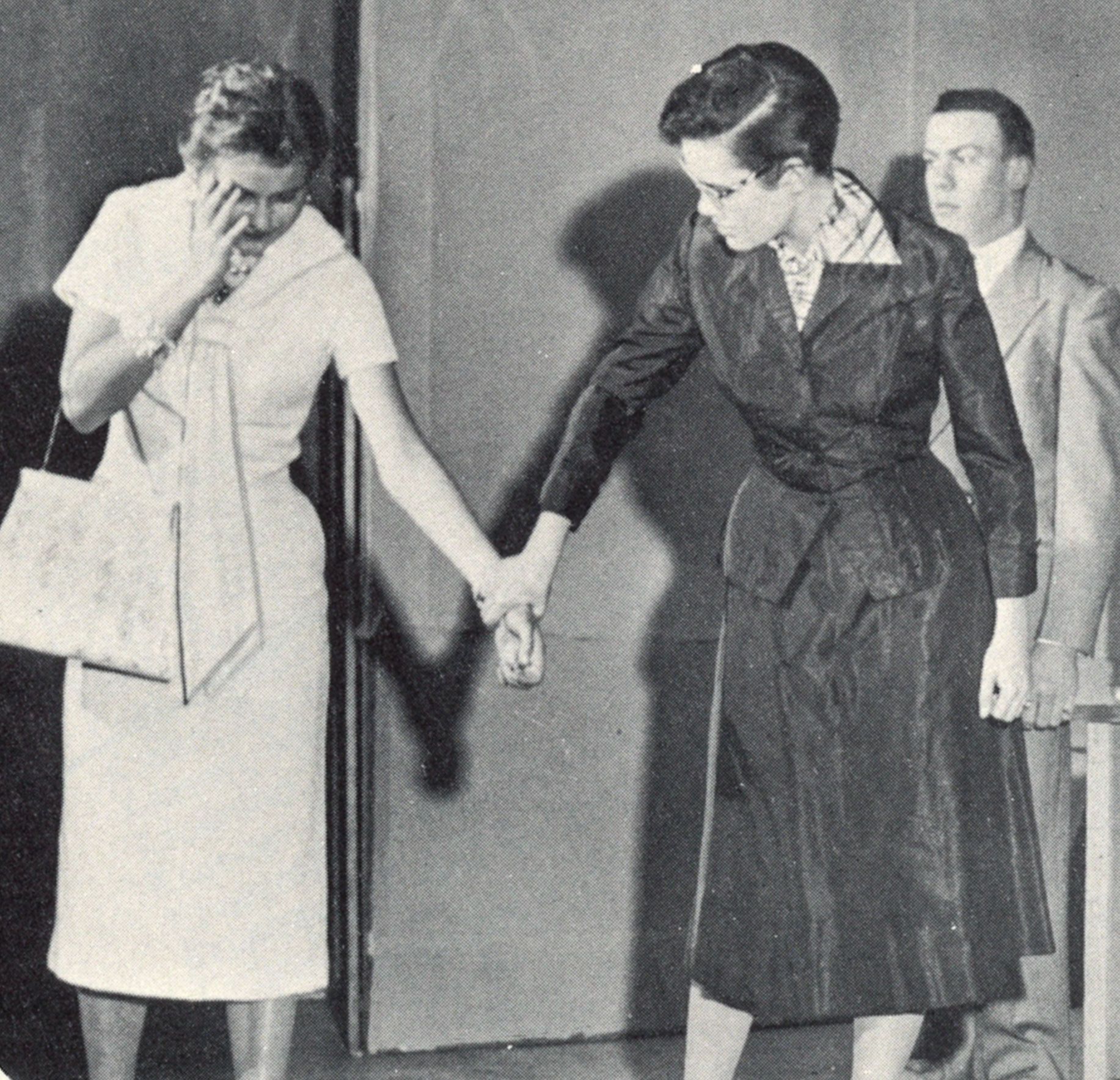 2 females in dresses, holding hands and looking down
