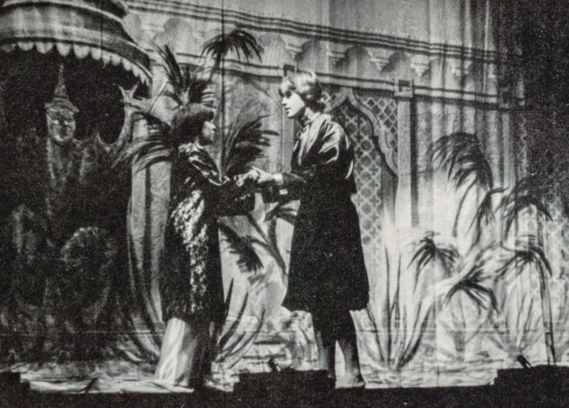 Male and female in robes, holding hands, with palm trees in background