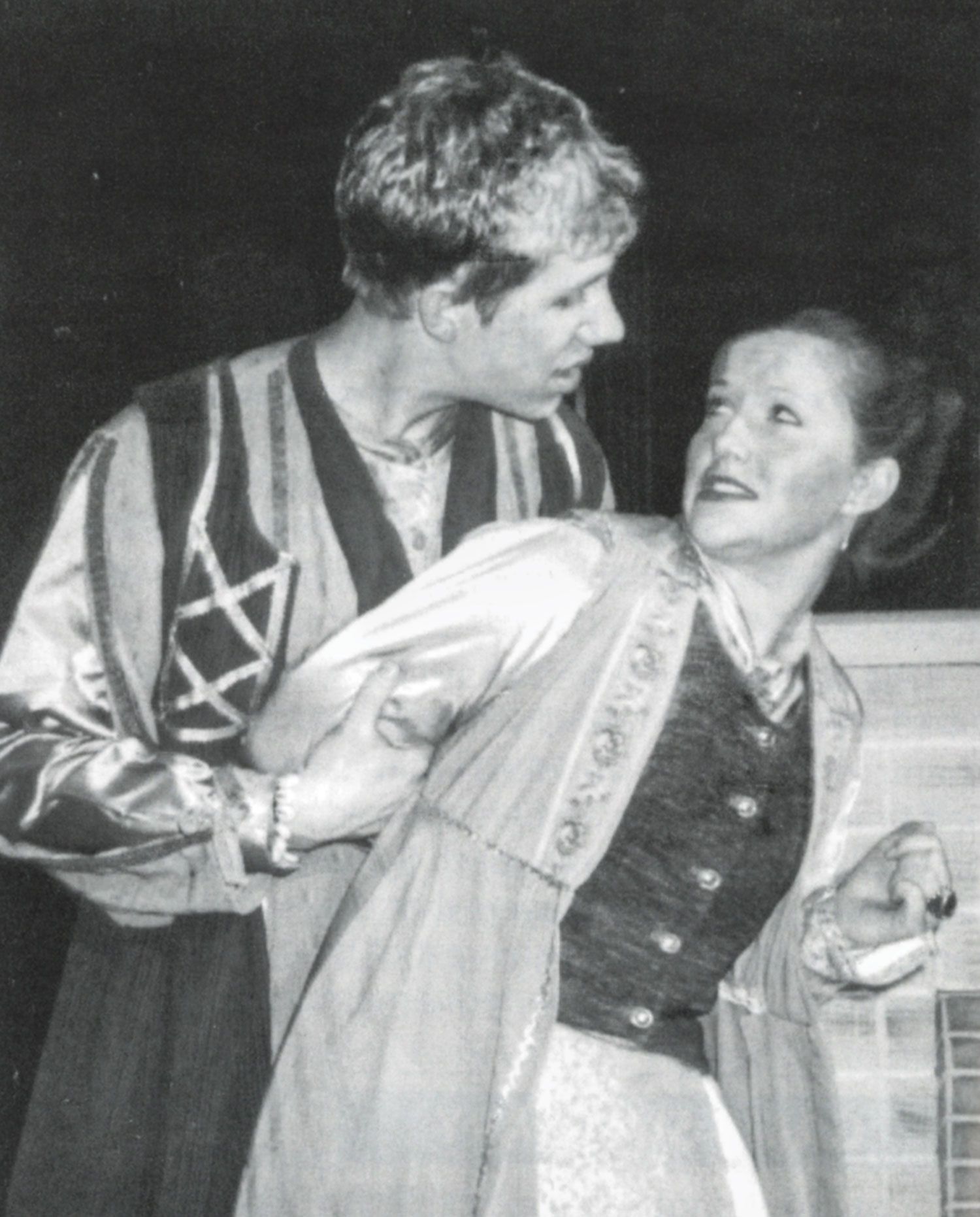 Female student with arms behind her back, looking at male student who is behind her, holding her arms