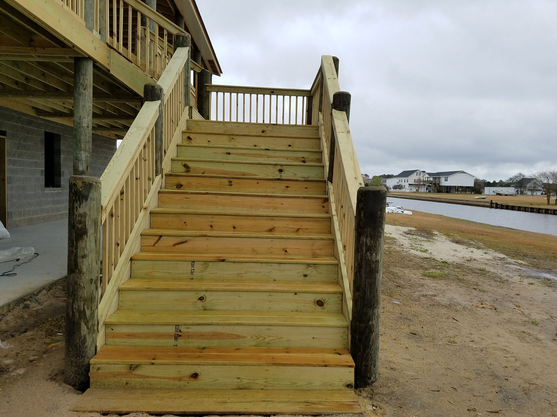 Wooden stairs leading to an elevated deck beside a sandy shoreline under cloudy skies