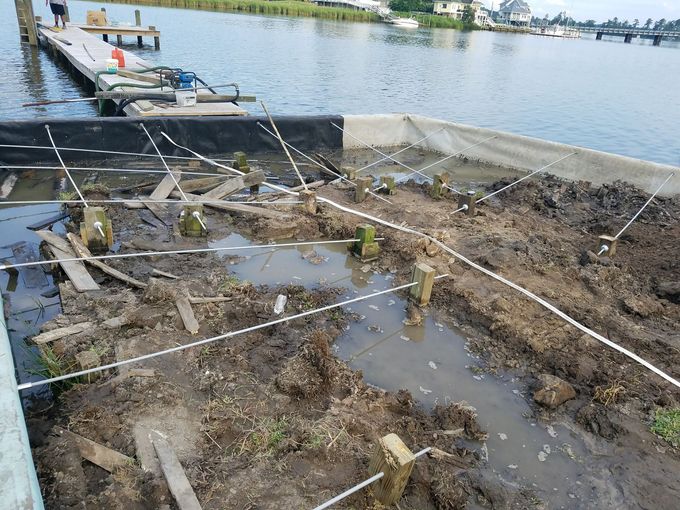 Flooded muddy construction site beside a calm lake with a dock and ropes in the foreground