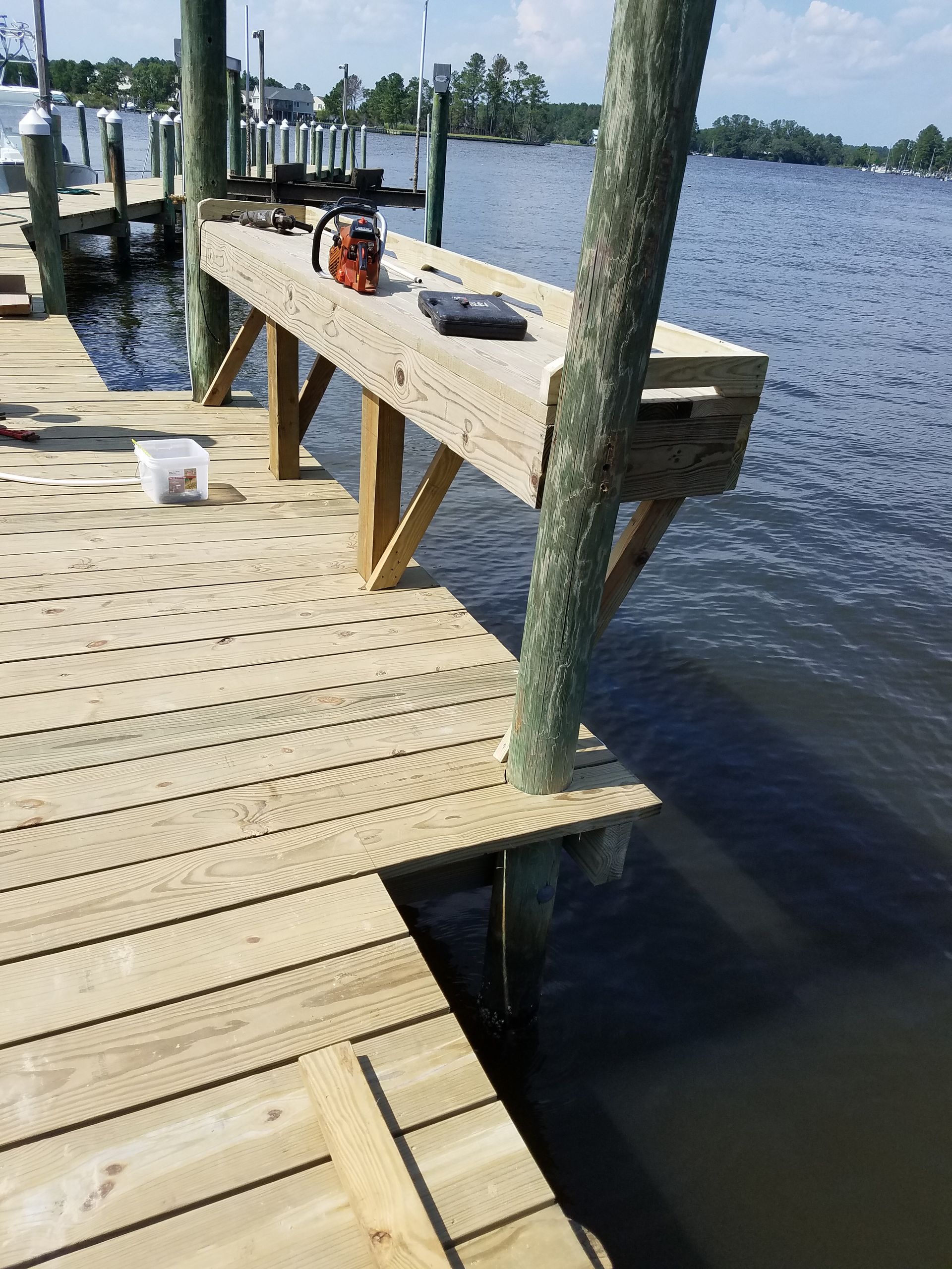 Wooden dock by a lake with a workbench, tools, and a T-shaped post over the water.