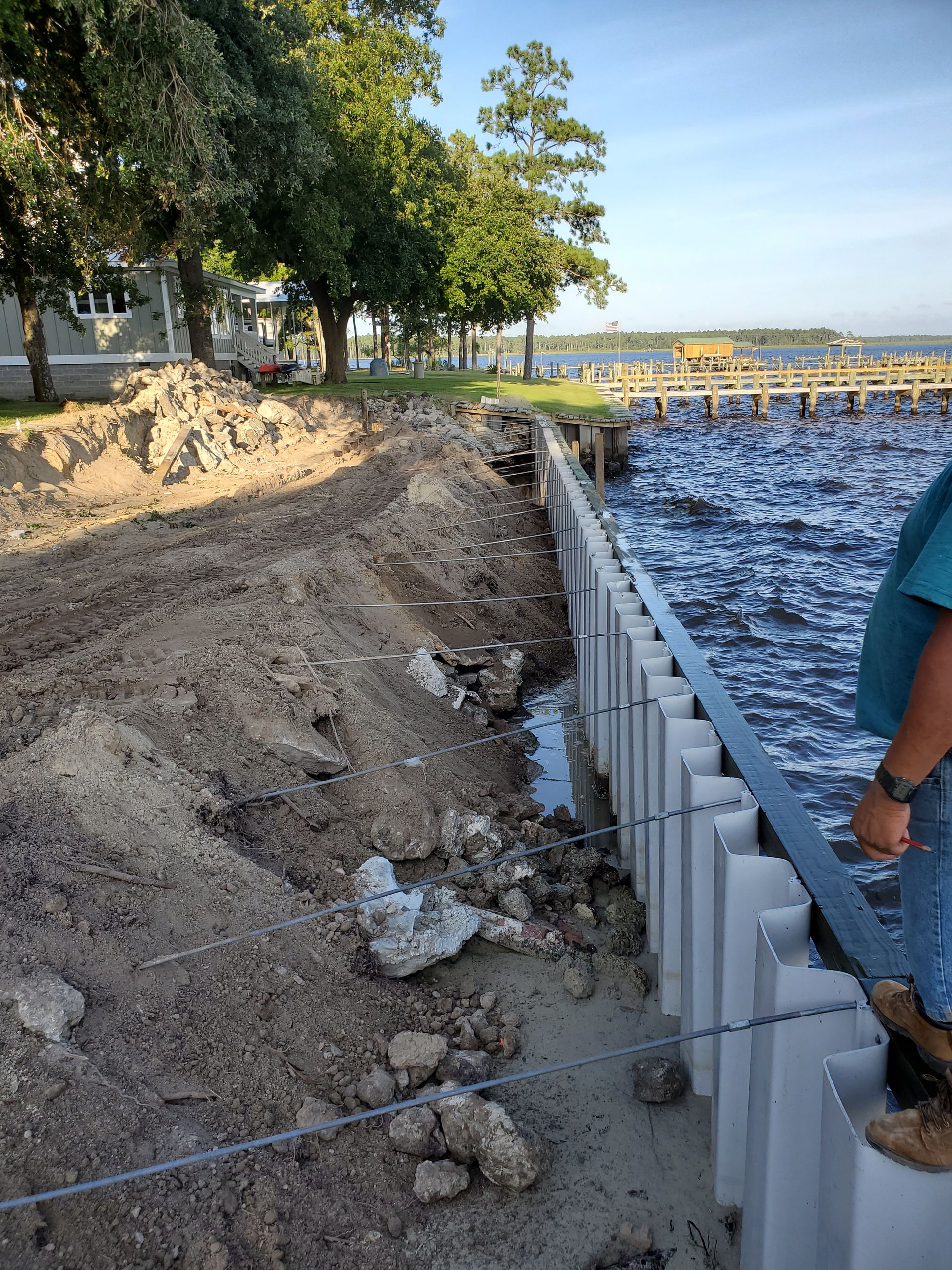 Shoreline erosion repair with white retaining wall beside muddy beach and choppy water