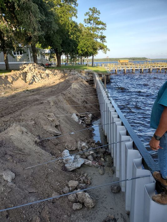 Shoreline erosion repair with white retaining wall beside muddy beach and choppy water