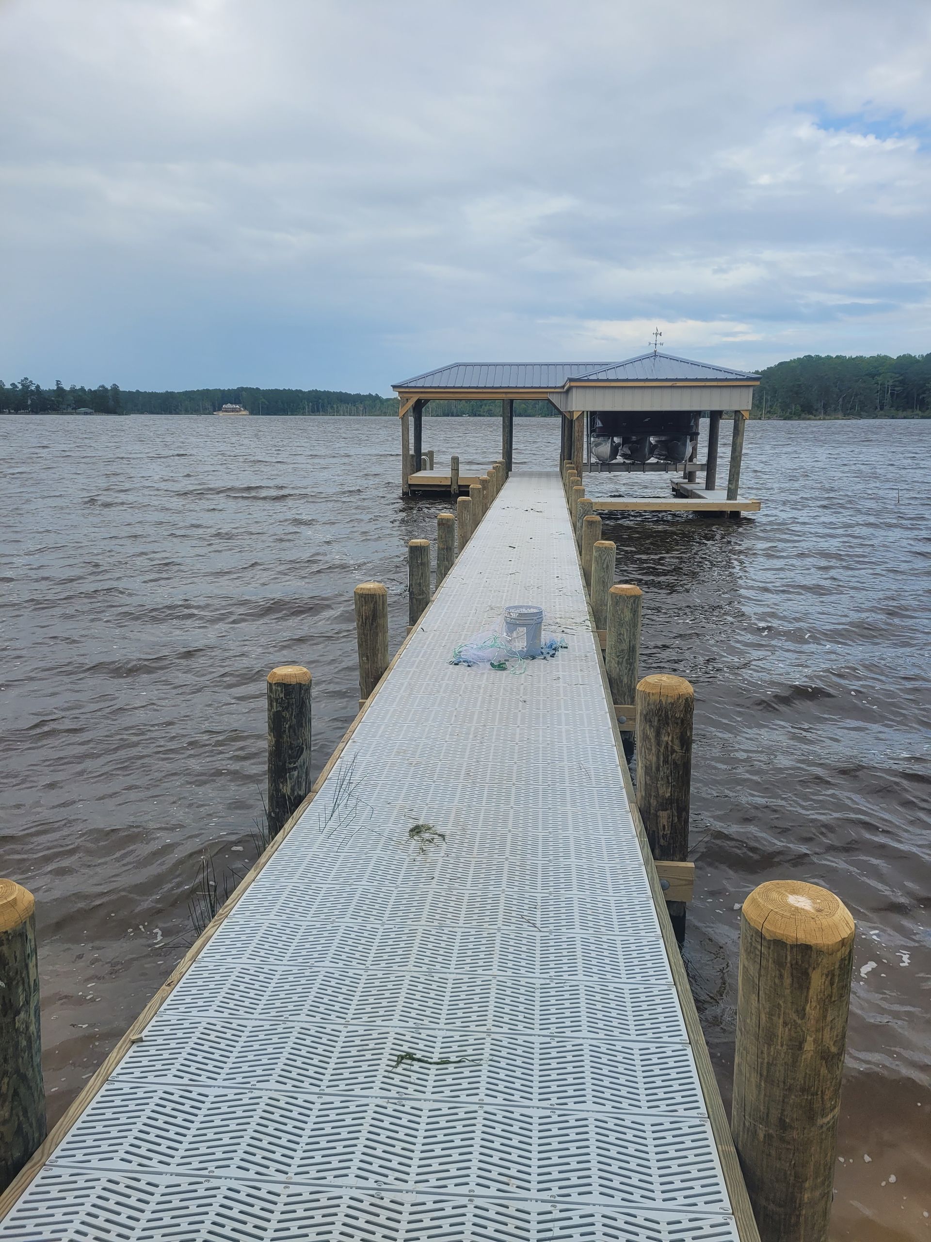 Snow-dusted dock leading to a lakeside gazebo under a cloudy sky