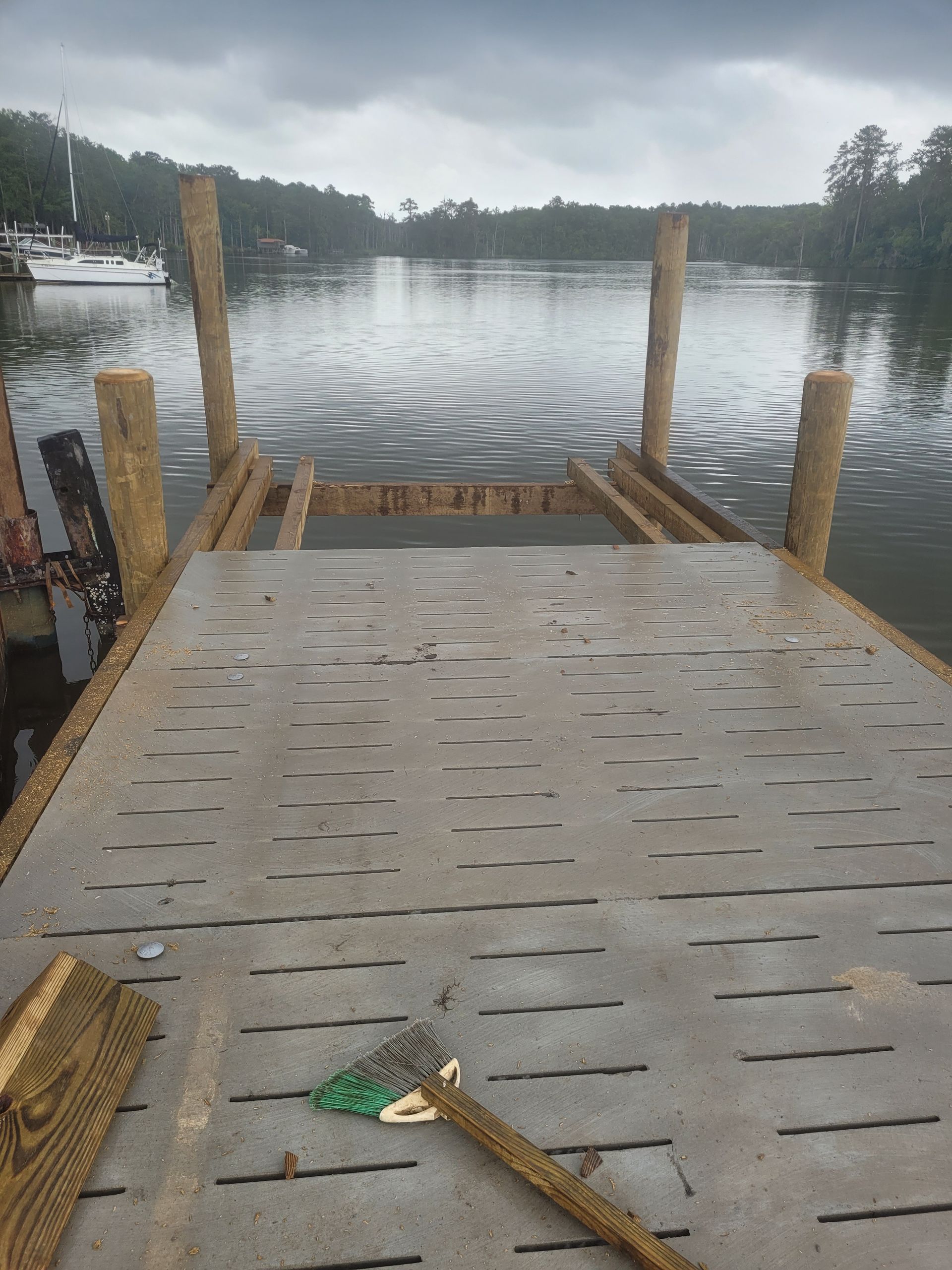 Wooden dock extending over a calm lake under a cloudy sky, with a fishing rod on the deck.