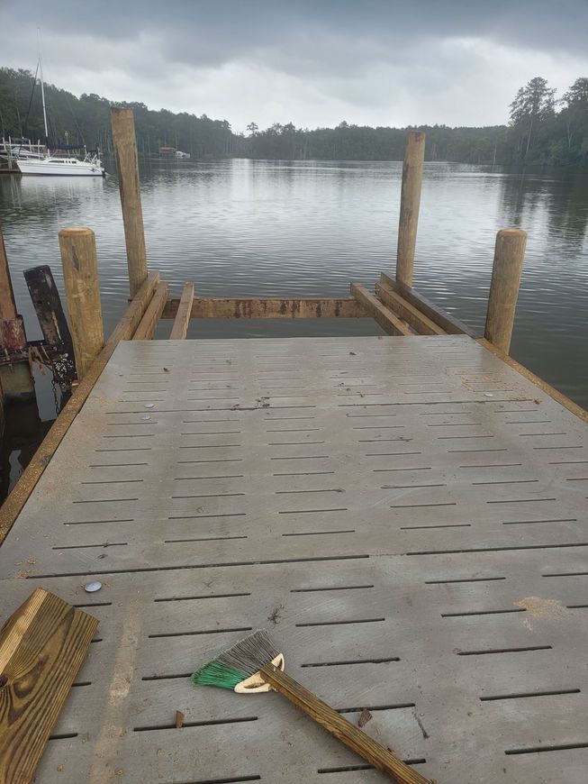 Riverside dock with weathered boards, leaning posts, and a calm lake under an overcast sky
