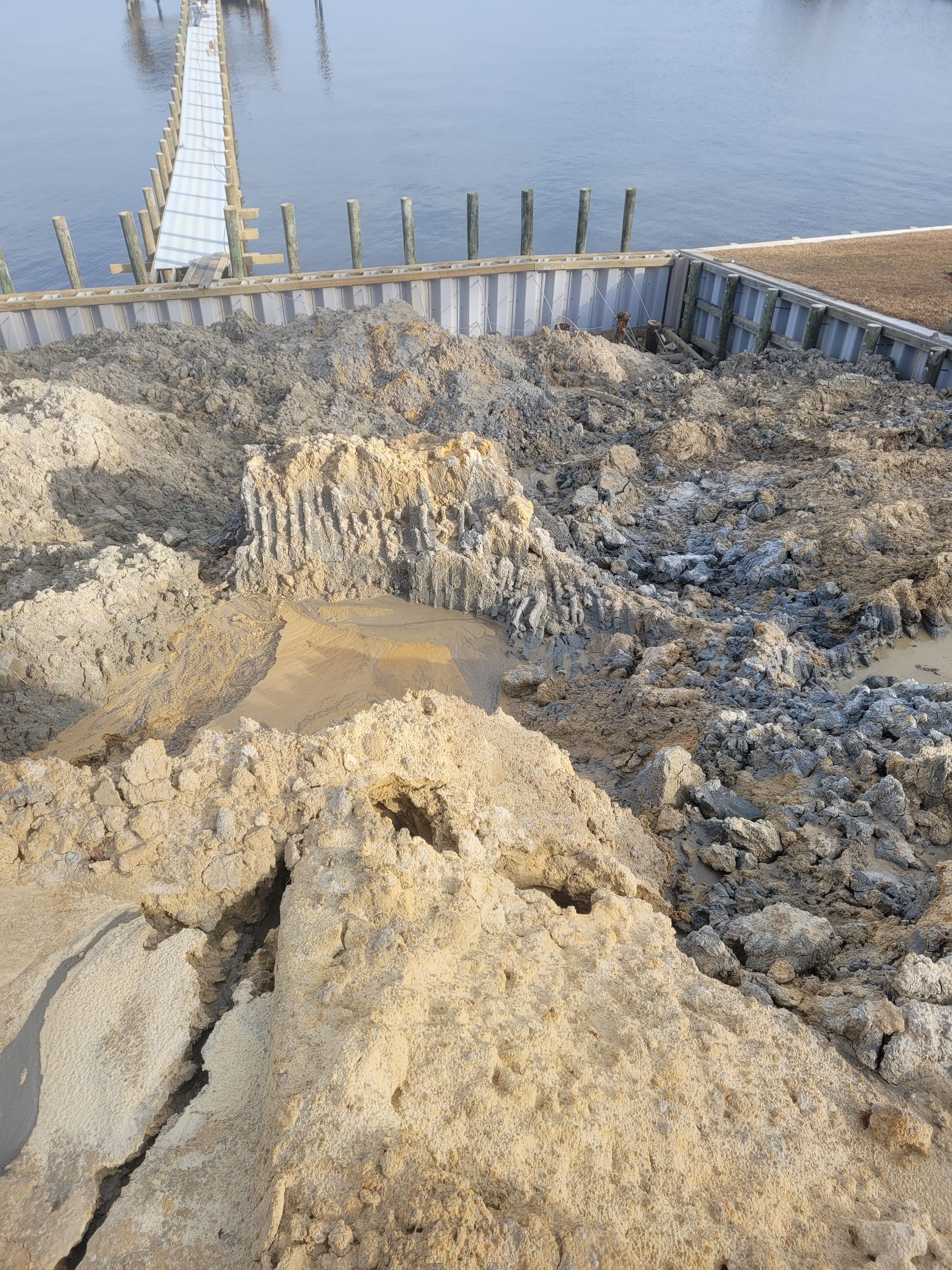 Piles of sand and gravel beside a calm waterfront dock with a white ladder and walkway