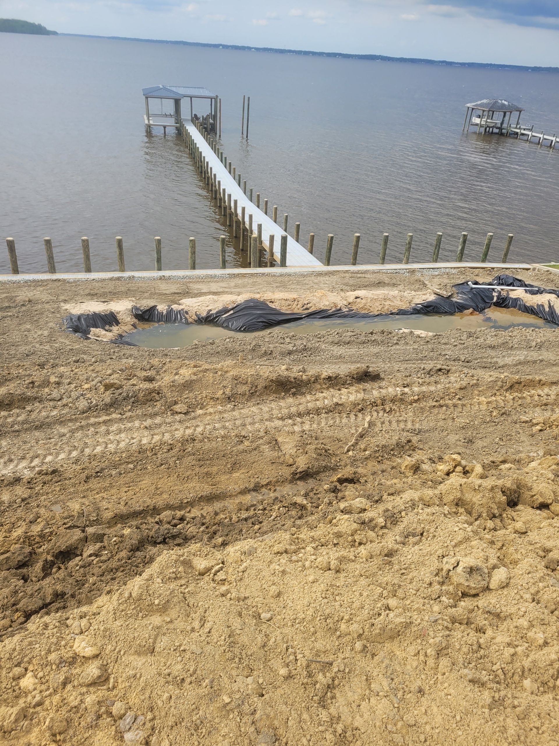 Sandy shoreline with a narrow dock extending into calm water under a gray sky