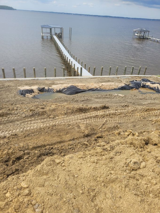 Sandy shoreline with a narrow dock extending into calm water under a gray sky