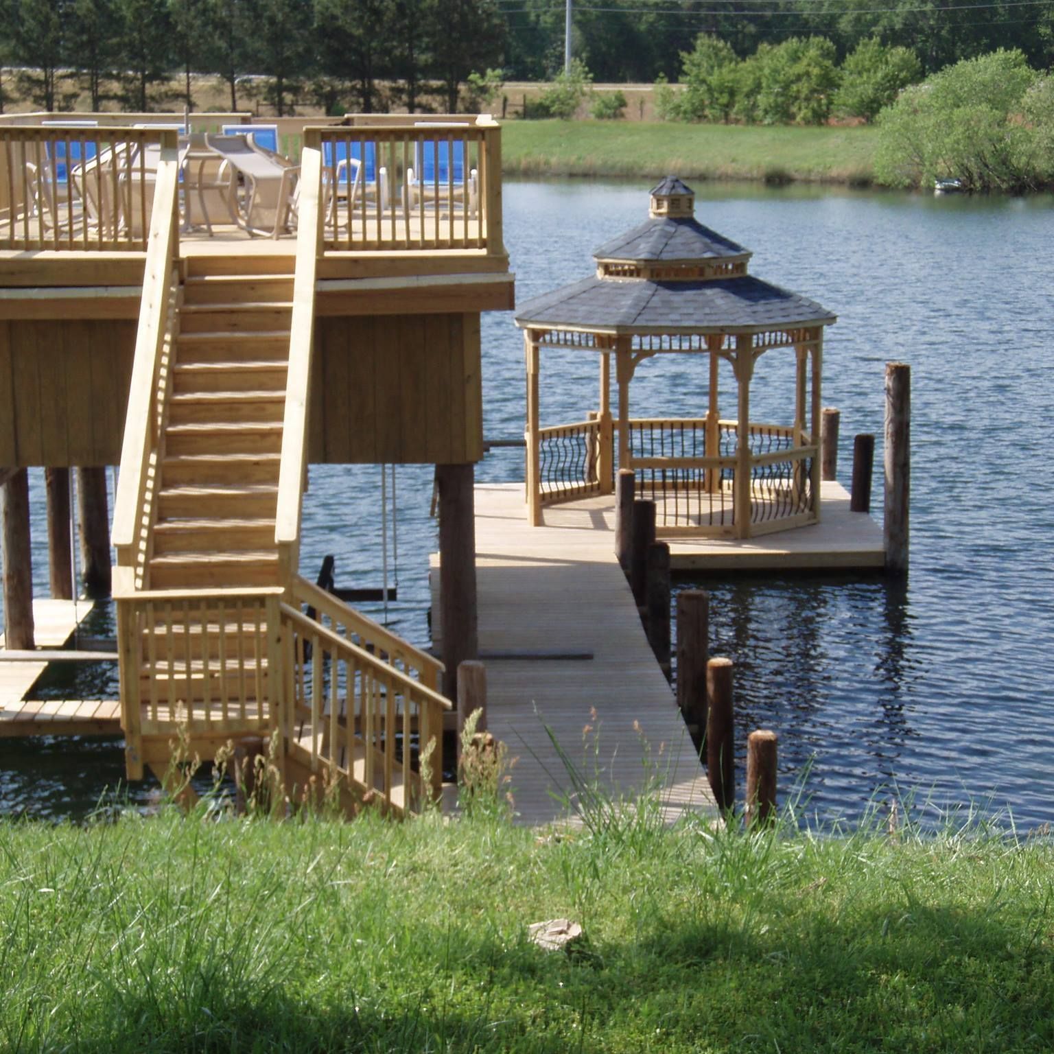 Wooden lakeside deck with stairs and a small gazebo over the water, bordered by green grass