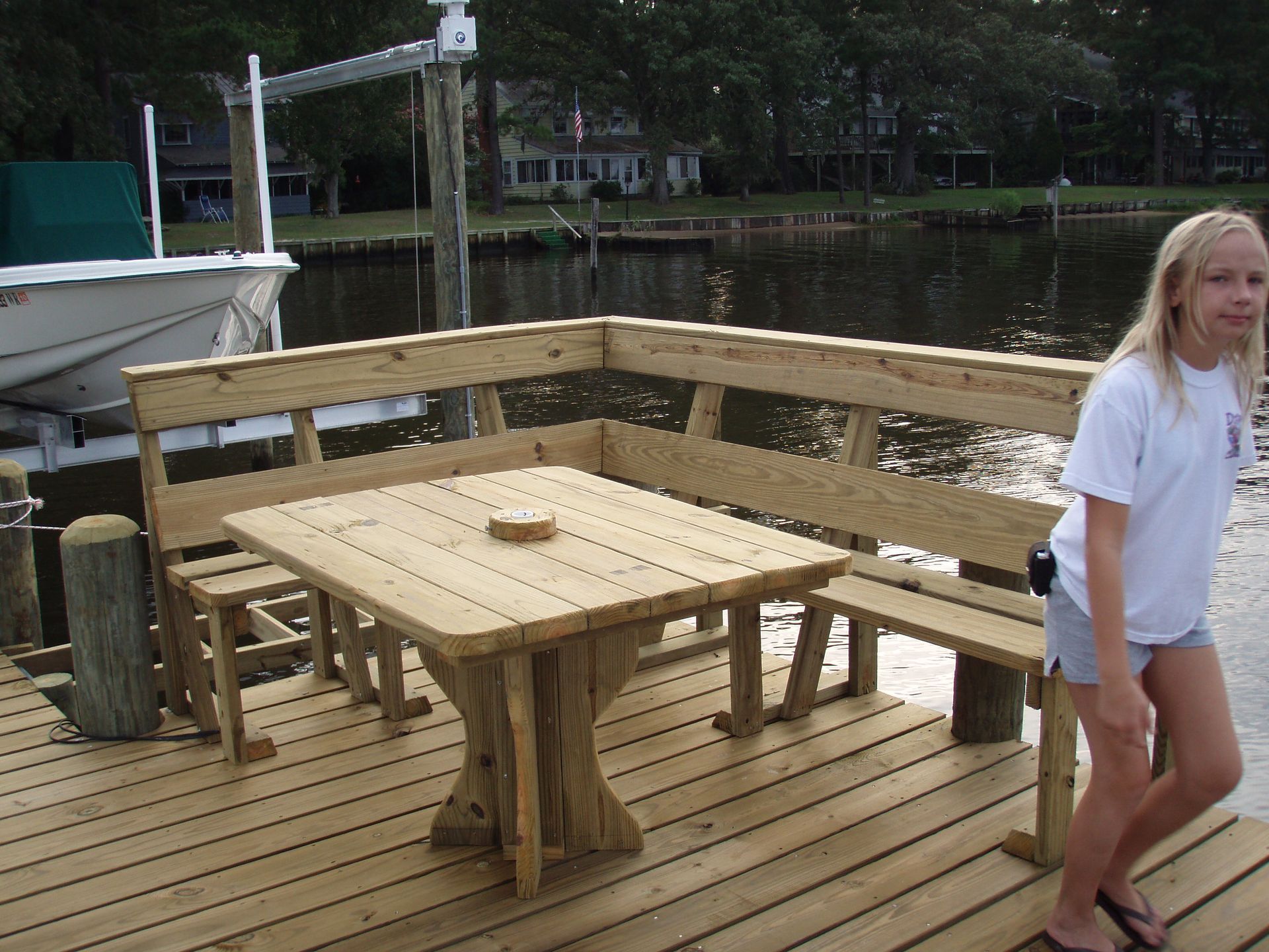 Wooden dock seating area by the water, with a table and benches beside a white boat.