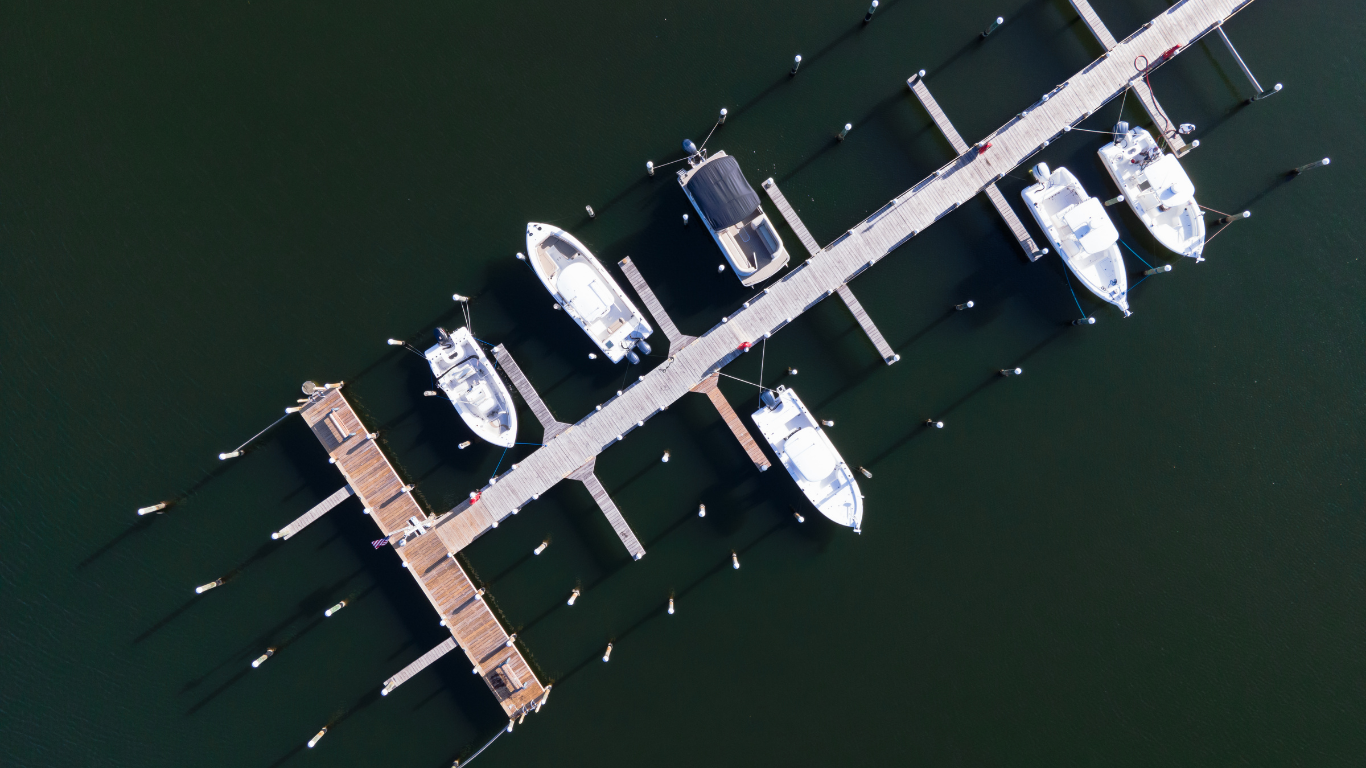 Aerial view of several boats docked along a floating marina on dark green water.